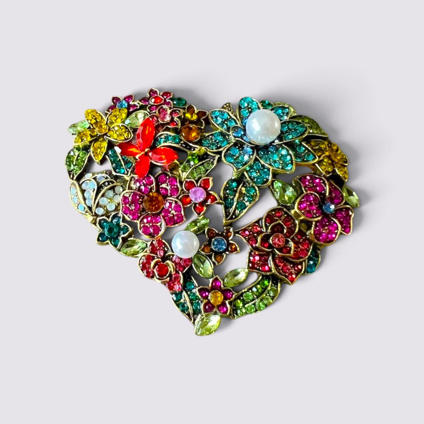 The Fashion Jewels heart-shaped brooch featuring multi-colored crystals, floral motifs, and faux pearl accents.