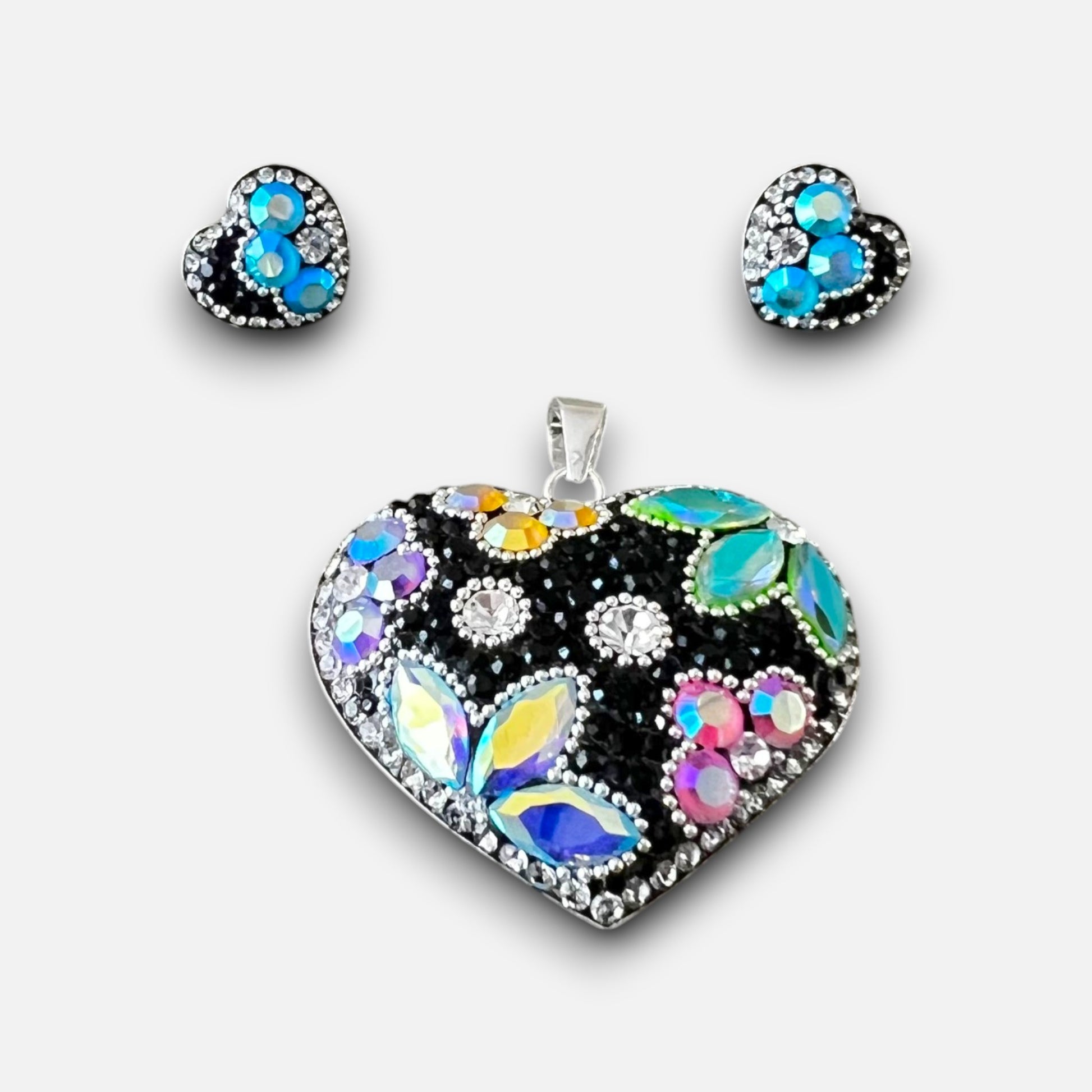 A heart-shaped jewelry set featuring a large pendant and matching stud earrings. The heart design is set in silver with a black background and decorated with iridescent, rainbow-colored rhinestones, blue stones, and clear crystals.