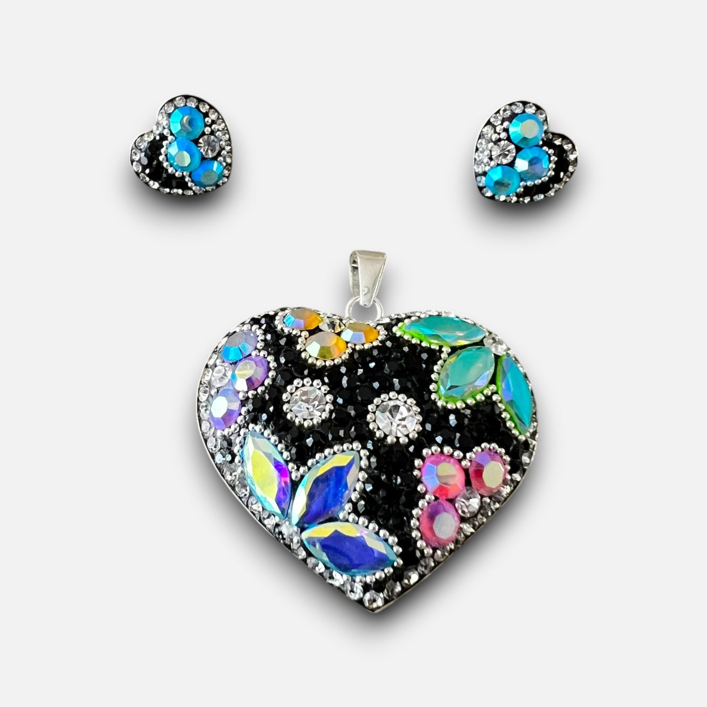 A heart-shaped pendant necklace and matching heart stud earrings set, featuring a black background embellished with iridescent blue, green, pink, and purple rhinestones, on a light gray background.