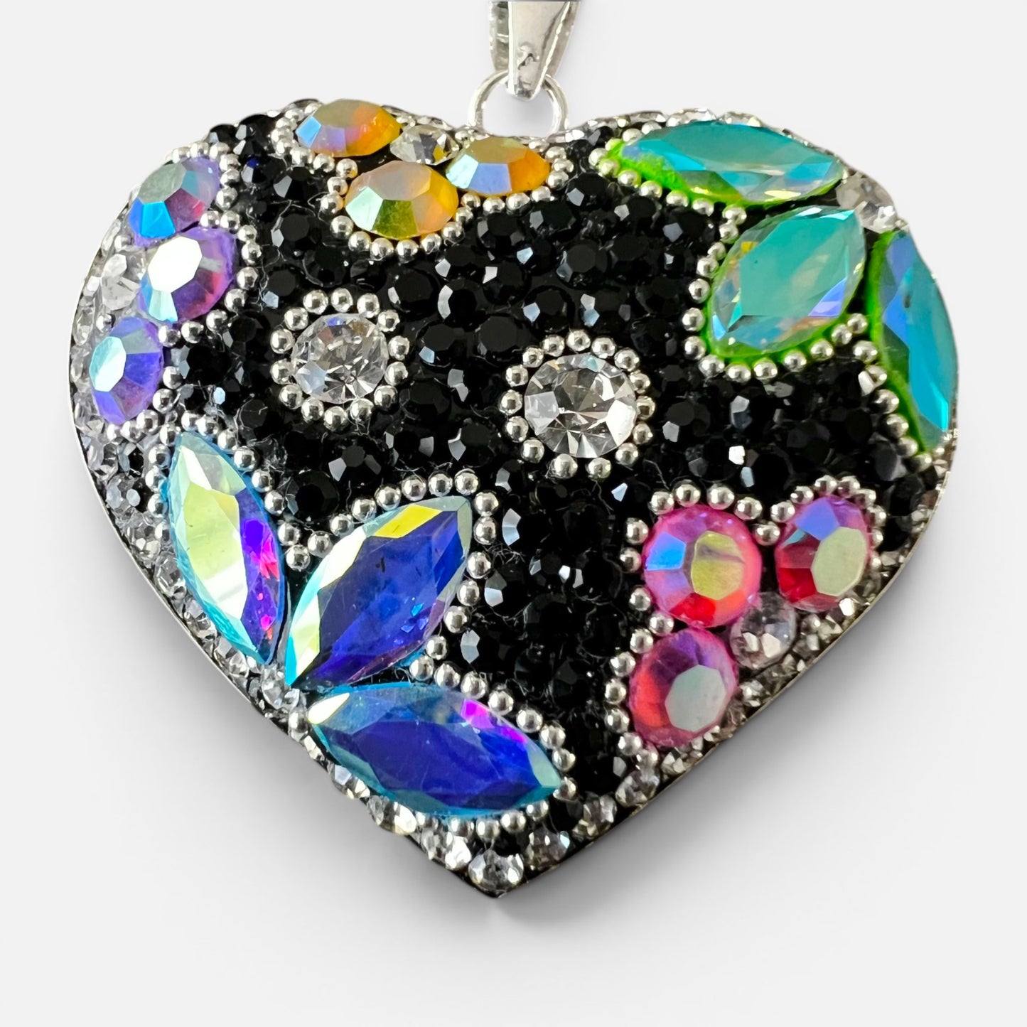 A heart-shaped pendant necklace featuring a black background paved with silver rhinestones, accented by iridescent blue, purple, pink, green, and orange crystals in a floral pattern.
