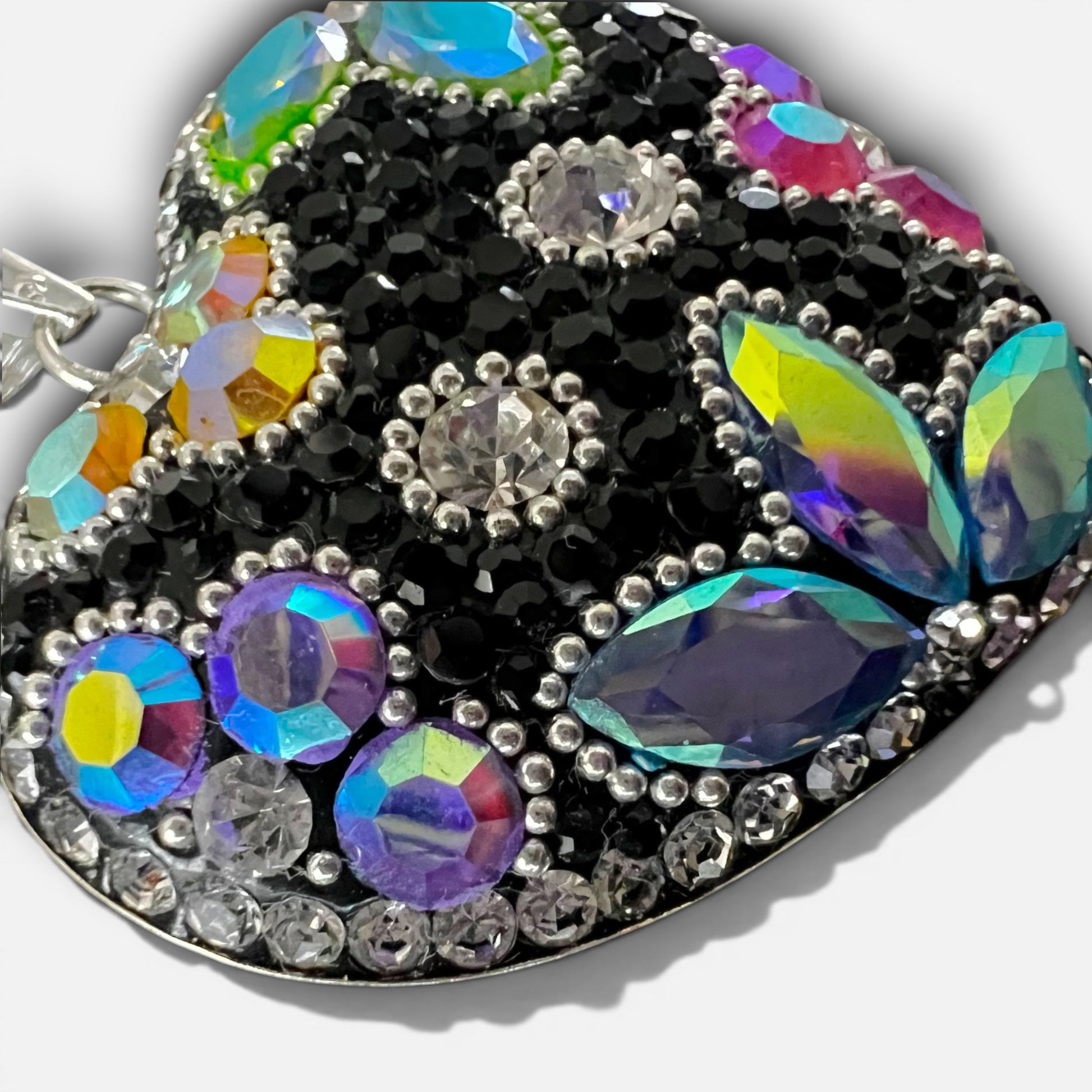 A heart-shaped rhinestone pendant featuring a black base embellished with iridescent, multicolored crystals and silver-tone settings, shown on a light gray background.