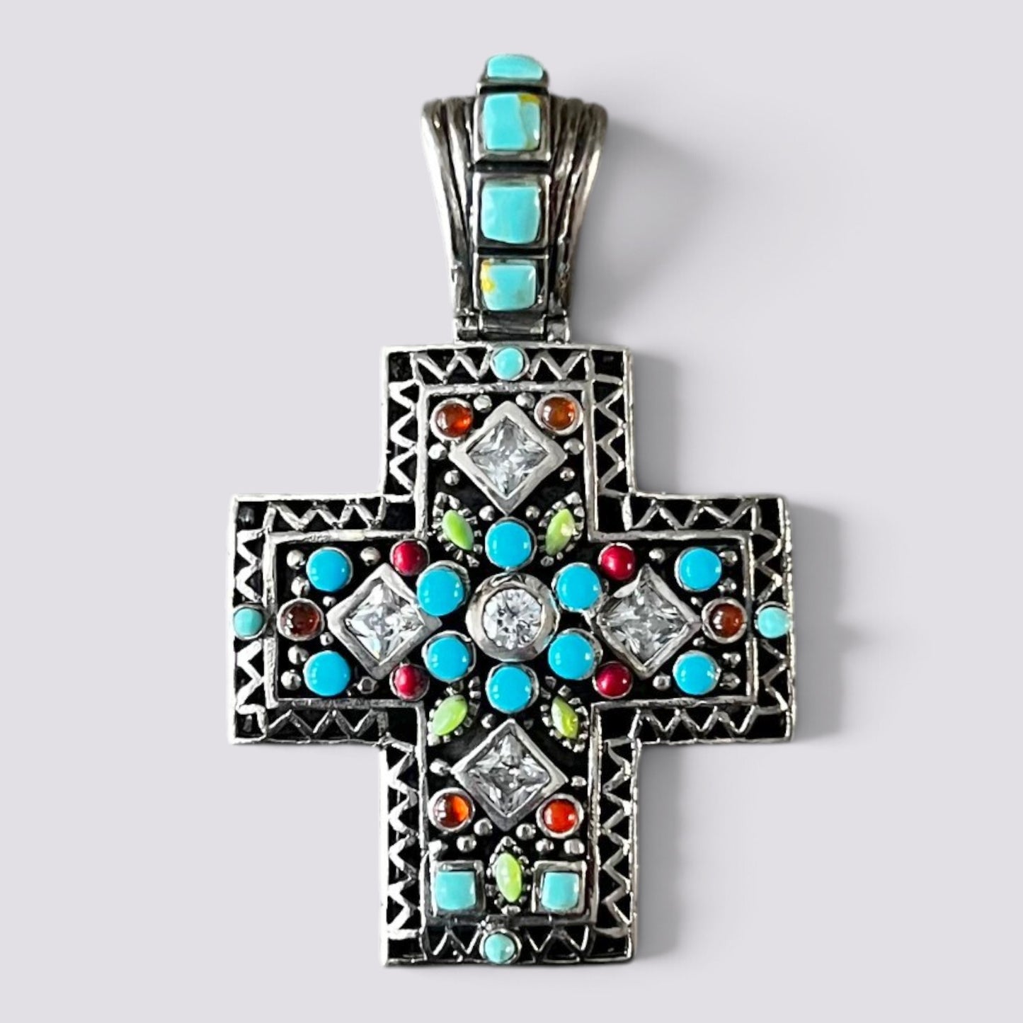 A silver-toned Orthodox cross pendant decorated with turquoise, red, green, and clear crystals, shown on a light gray background.
