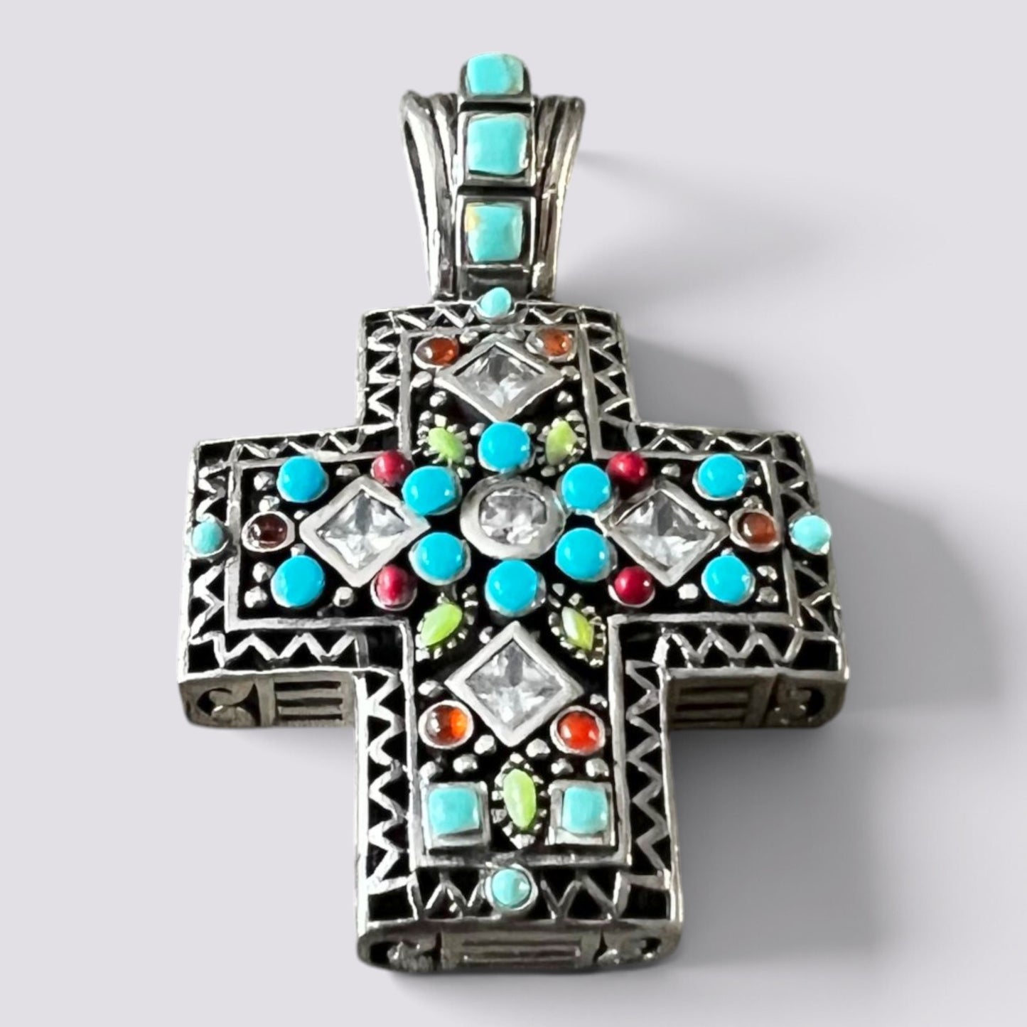 A silver-toned Orthodox cross pendant decorated with turquoise, red, green, and clear stones, shown on a light gray background.