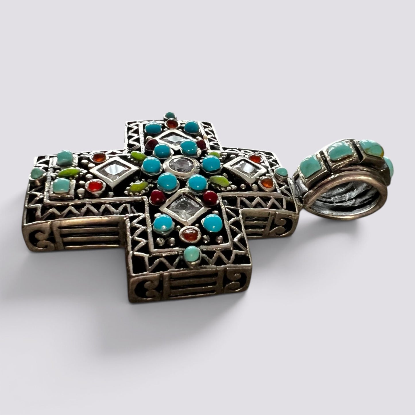 An ornate silver-toned Orthodox cross pendant decorated with turquoise, red, green, and clear stones, shown alongside a matching silver ring on a light gray background.