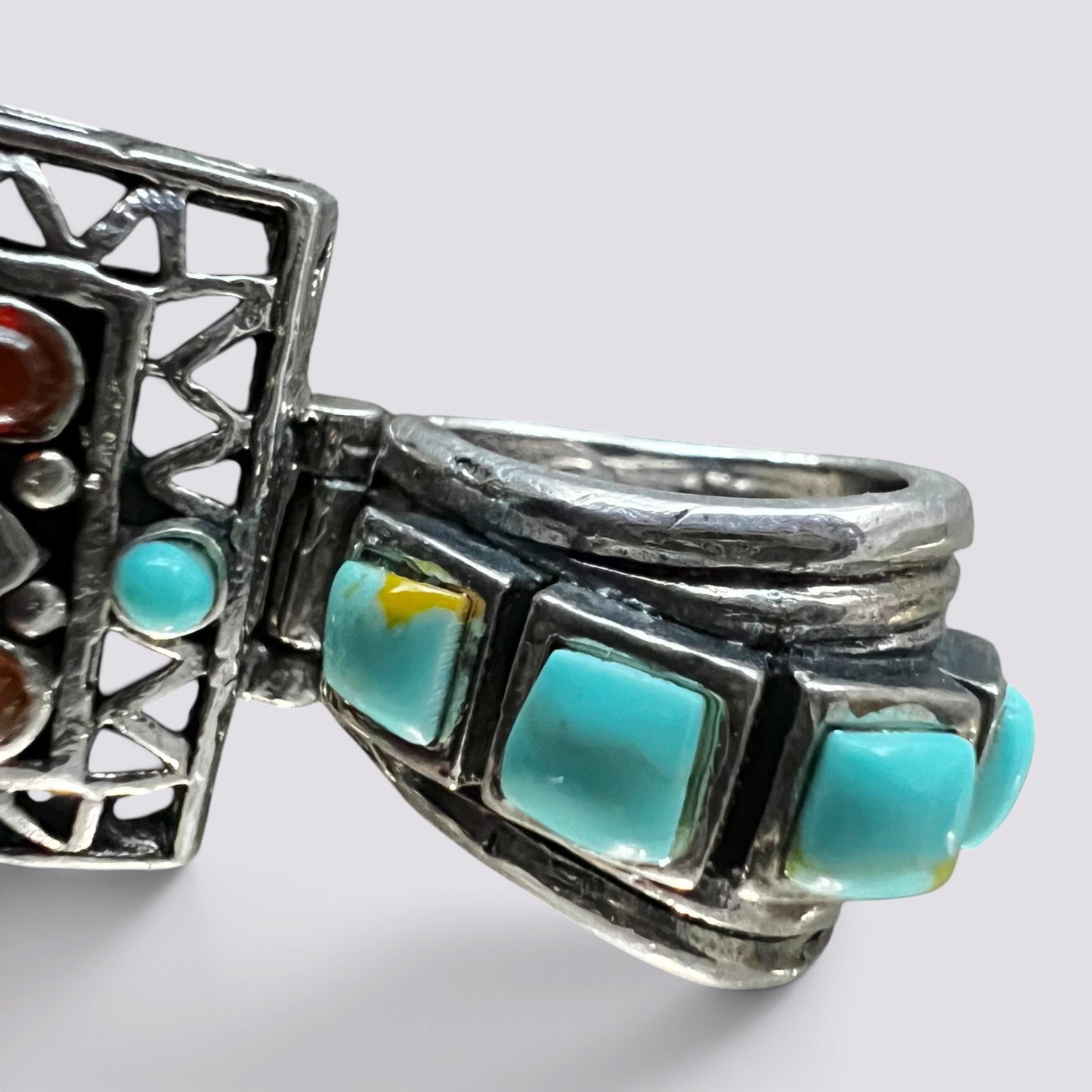 A close-up of a silver-toned ring featuring multiple rectangular turquoise stones and a smaller round turquoise accent, set against a plain light gray background.