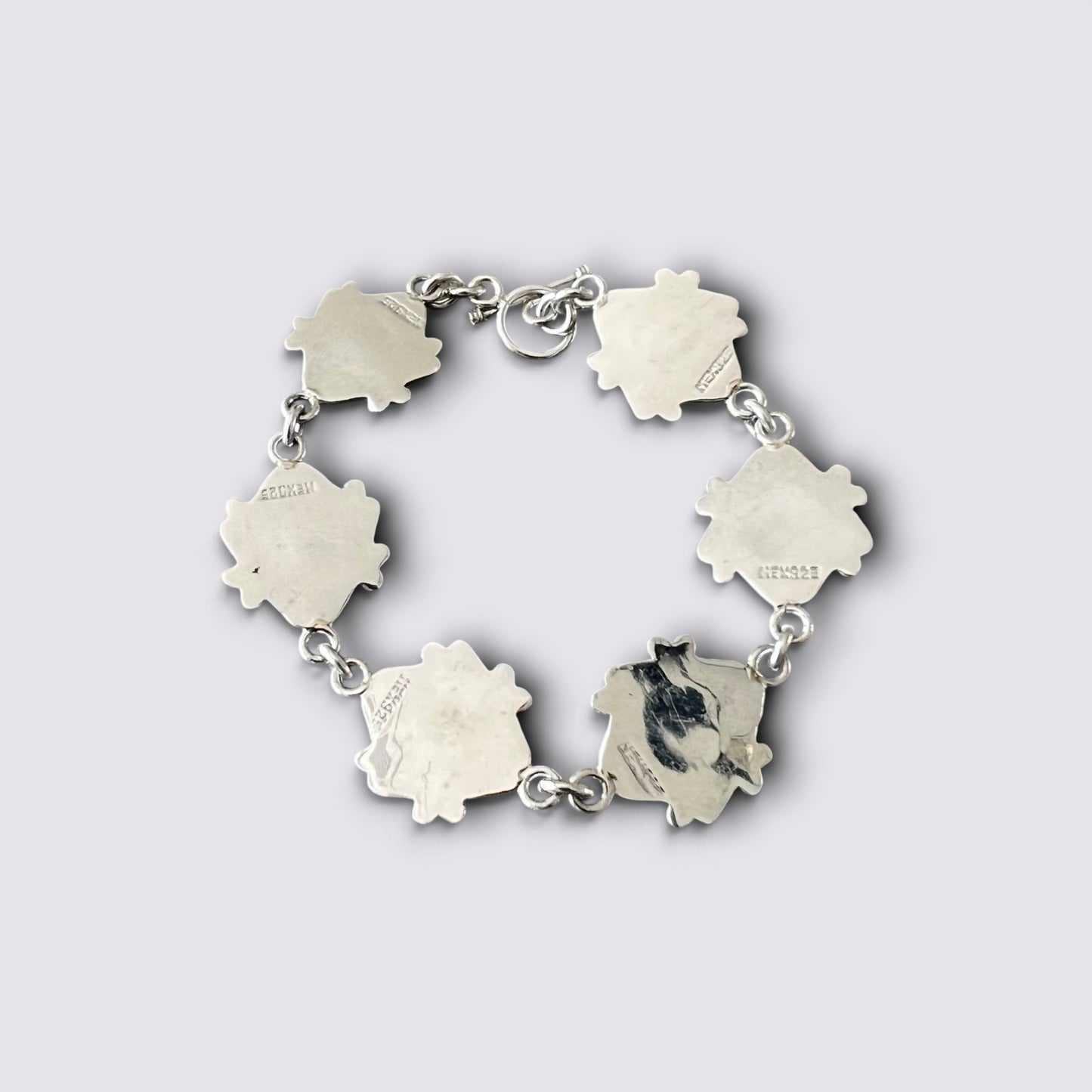 A silver-toned link bracelet featuring five irregular, petal-like charms, with one charm showing a black-and-white cat portrait and others engraved with small text, set against a light gray background.