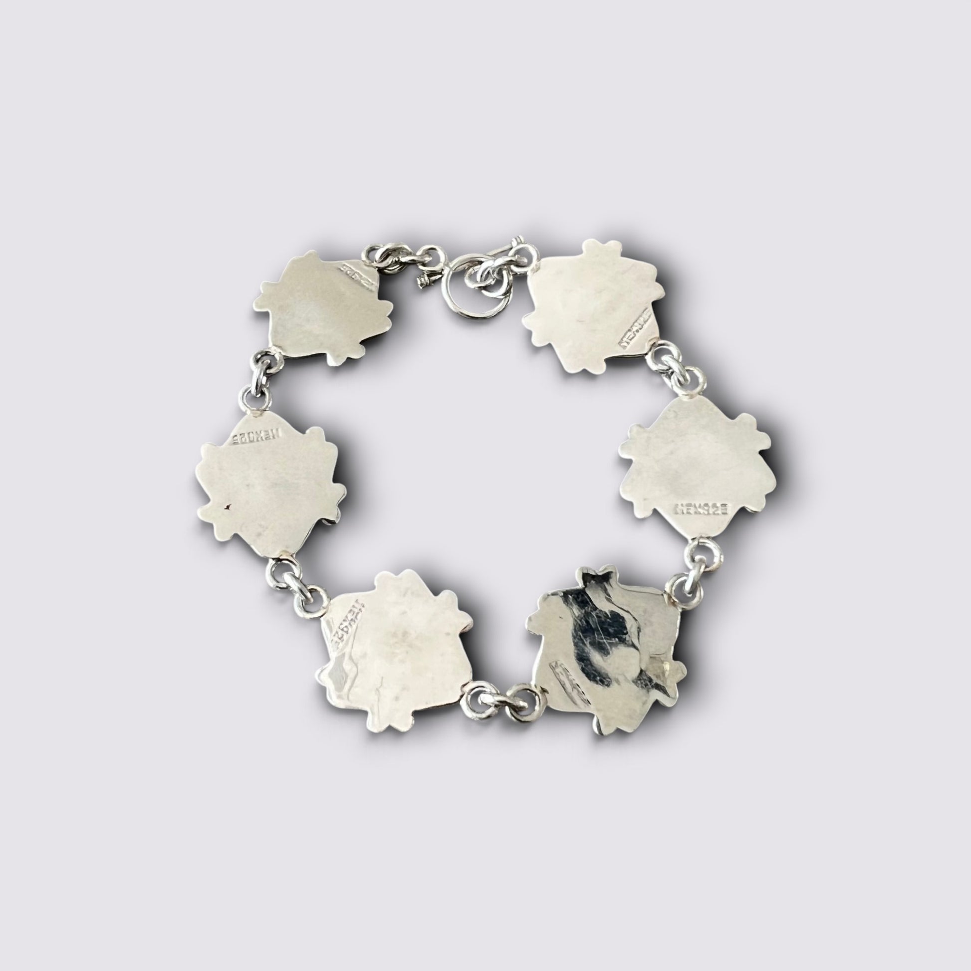 A silver-toned link bracelet featuring five irregular, petal-like charms, with one charm showing a black-and-white cat portrait and others engraved with small text, set against a light gray background.