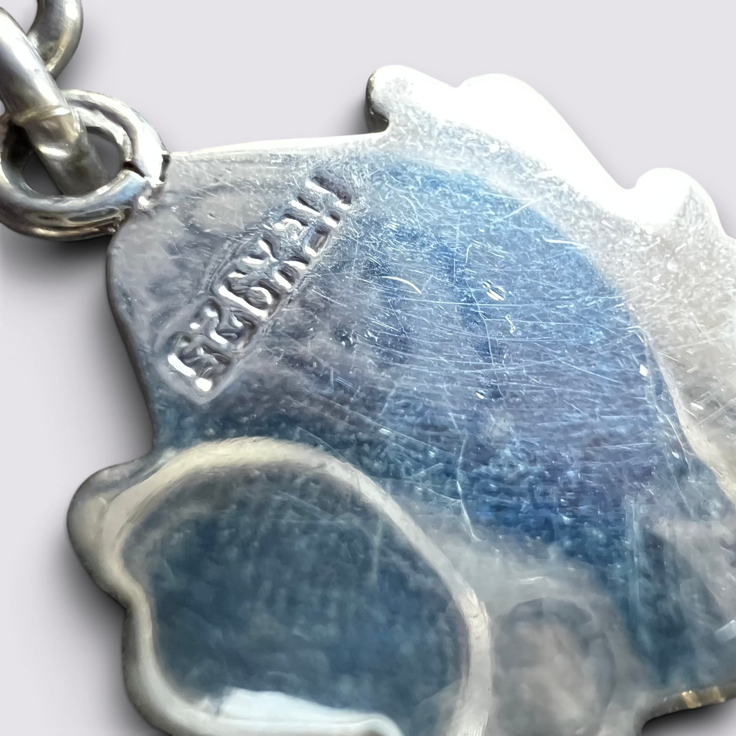 Close-up of a silver dog-shaped pendant charm with a blue inlay, showing the brand name 'HESKULL' stamped on the side and a silver clasp at the top left.