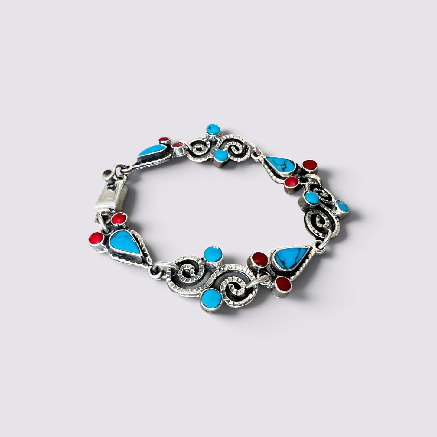 A silver-toned bracelet featuring turquoise blue and red inlay stones, photographed on a light gray background.