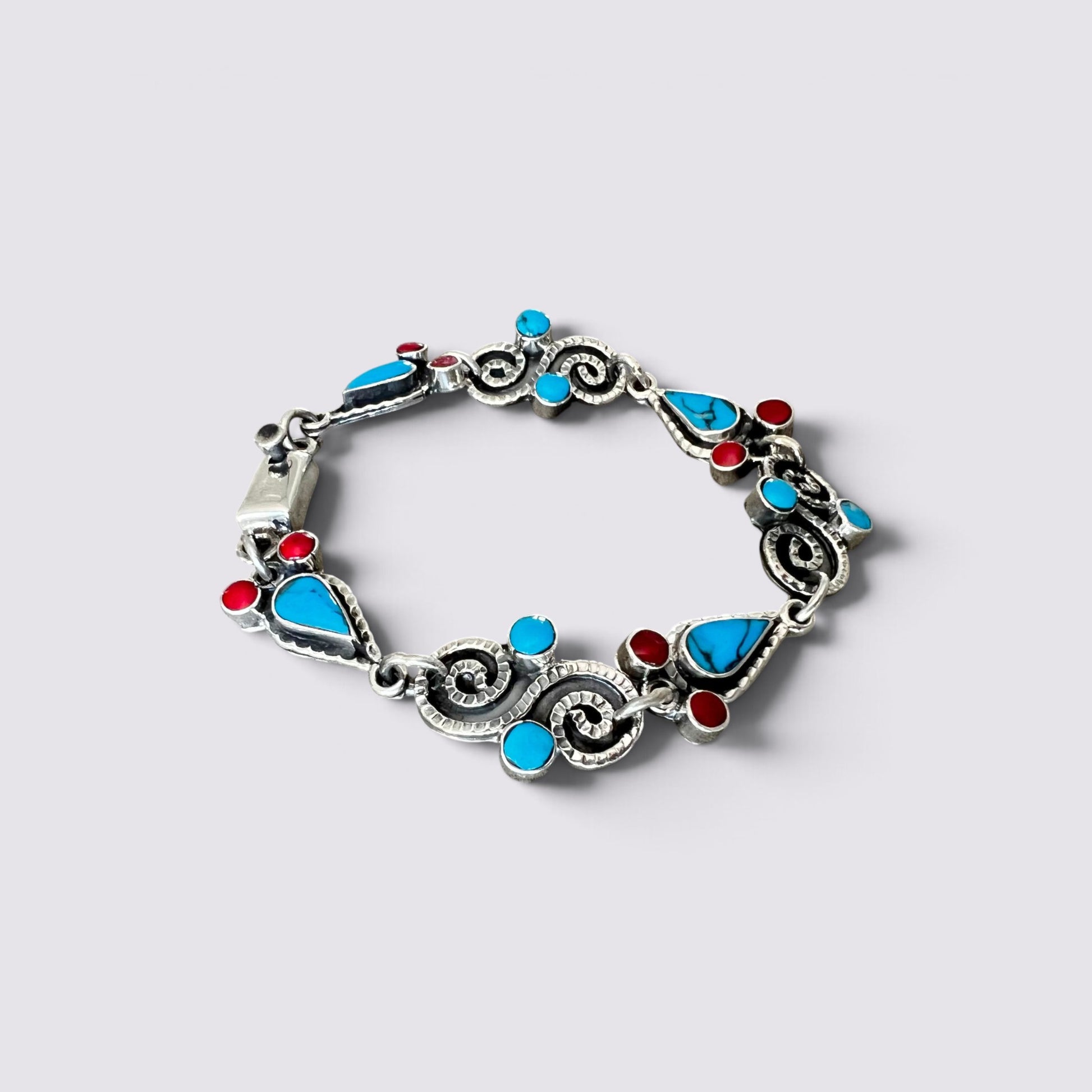 A silver-toned bracelet featuring turquoise blue and red inlay stones, photographed on a light gray background.