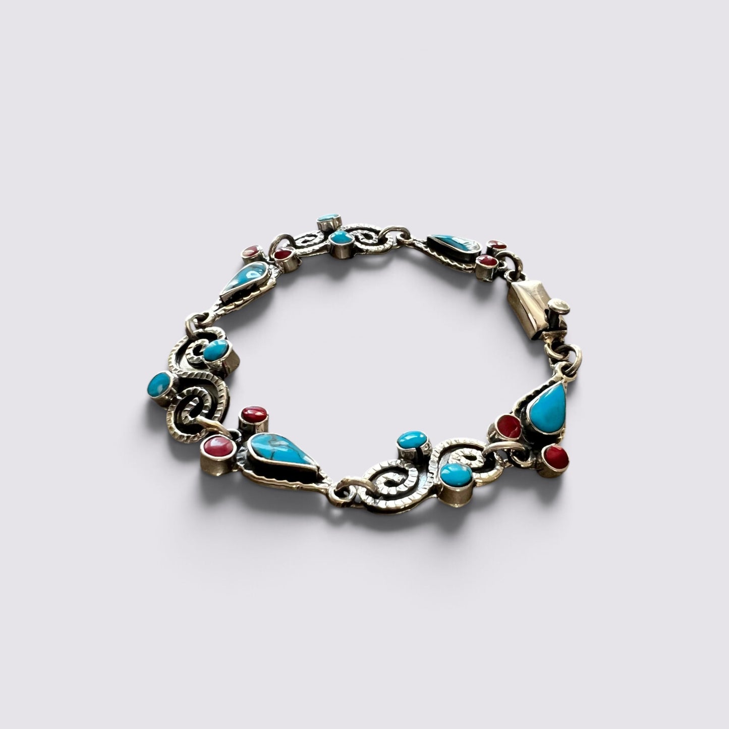 An ornate silver-toned bracelet featuring turquoise, red, and blue gemstone accents, displayed on a light gray background.