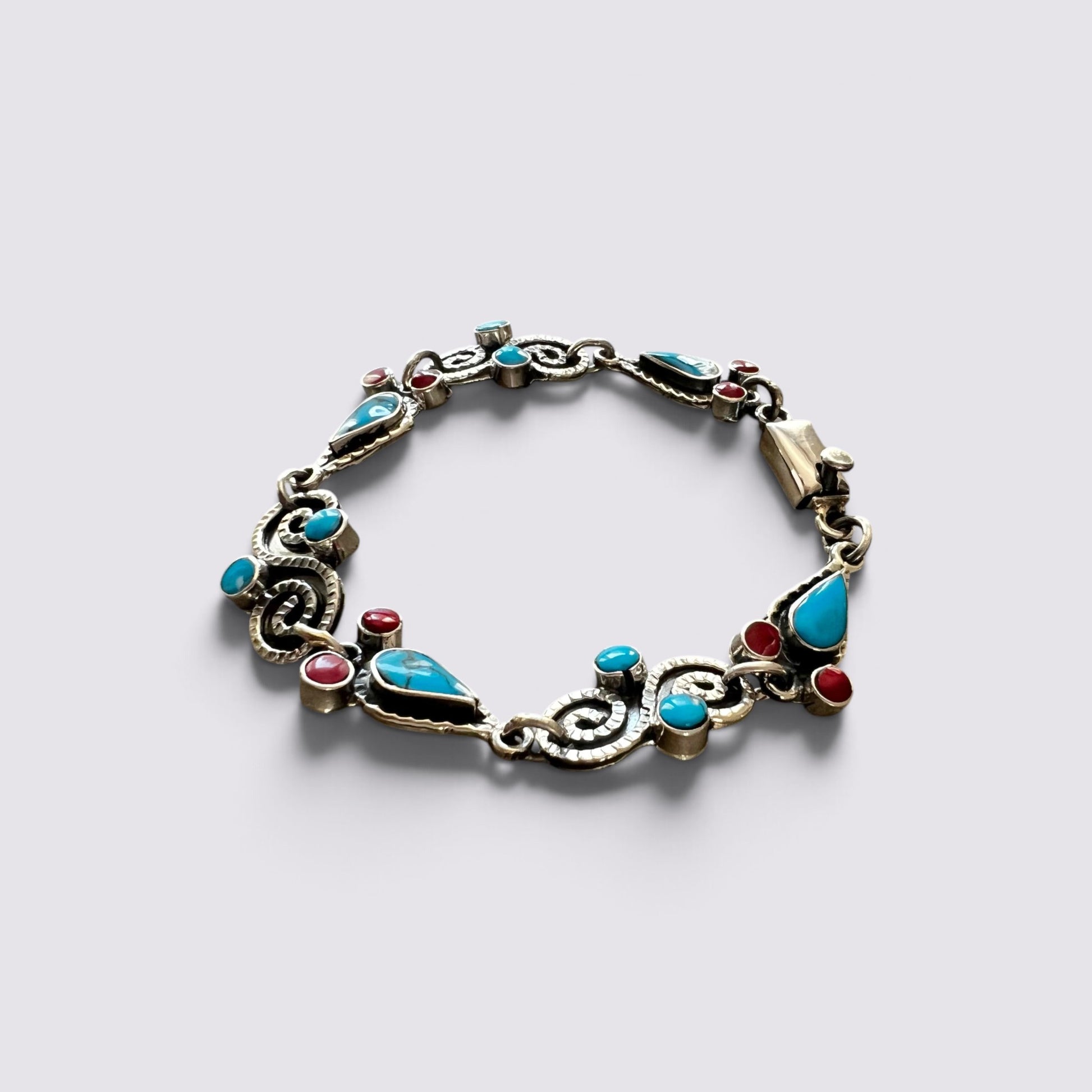 An ornate silver-toned bracelet featuring turquoise, red, and blue gemstone accents, displayed on a light gray background.