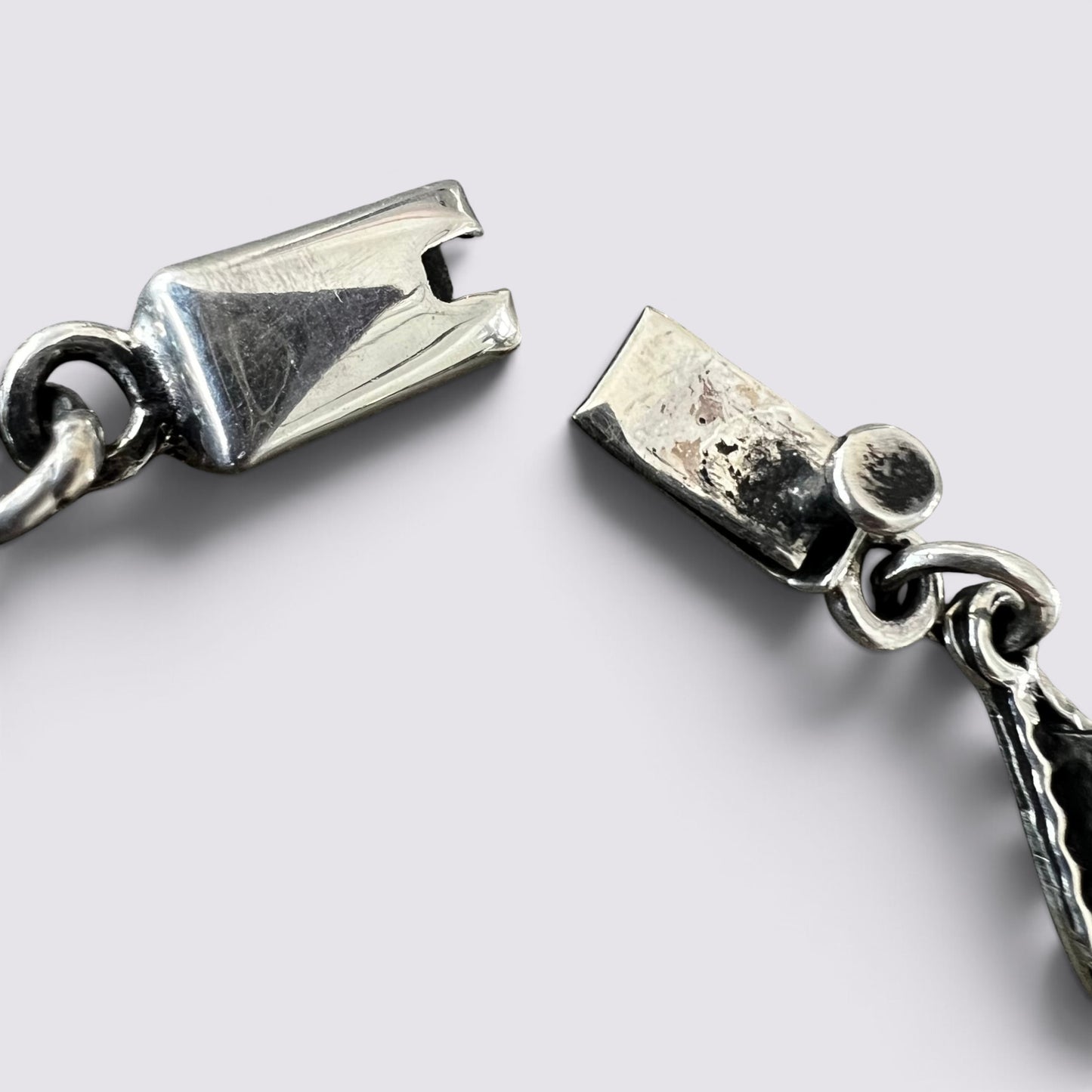 Close-up of a silver-toned metal zipper pull and chain on a light gray background.