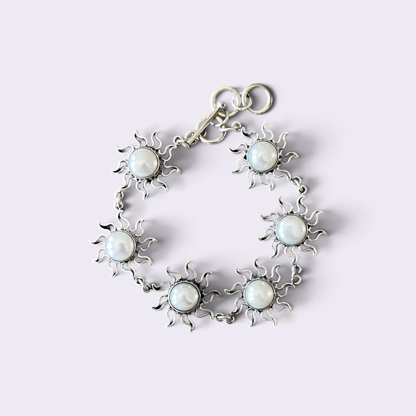 A silver-toned bracelet featuring six sunburst motifs, each with a round white faux-pearl center, arranged in a circle on a light lavender background.