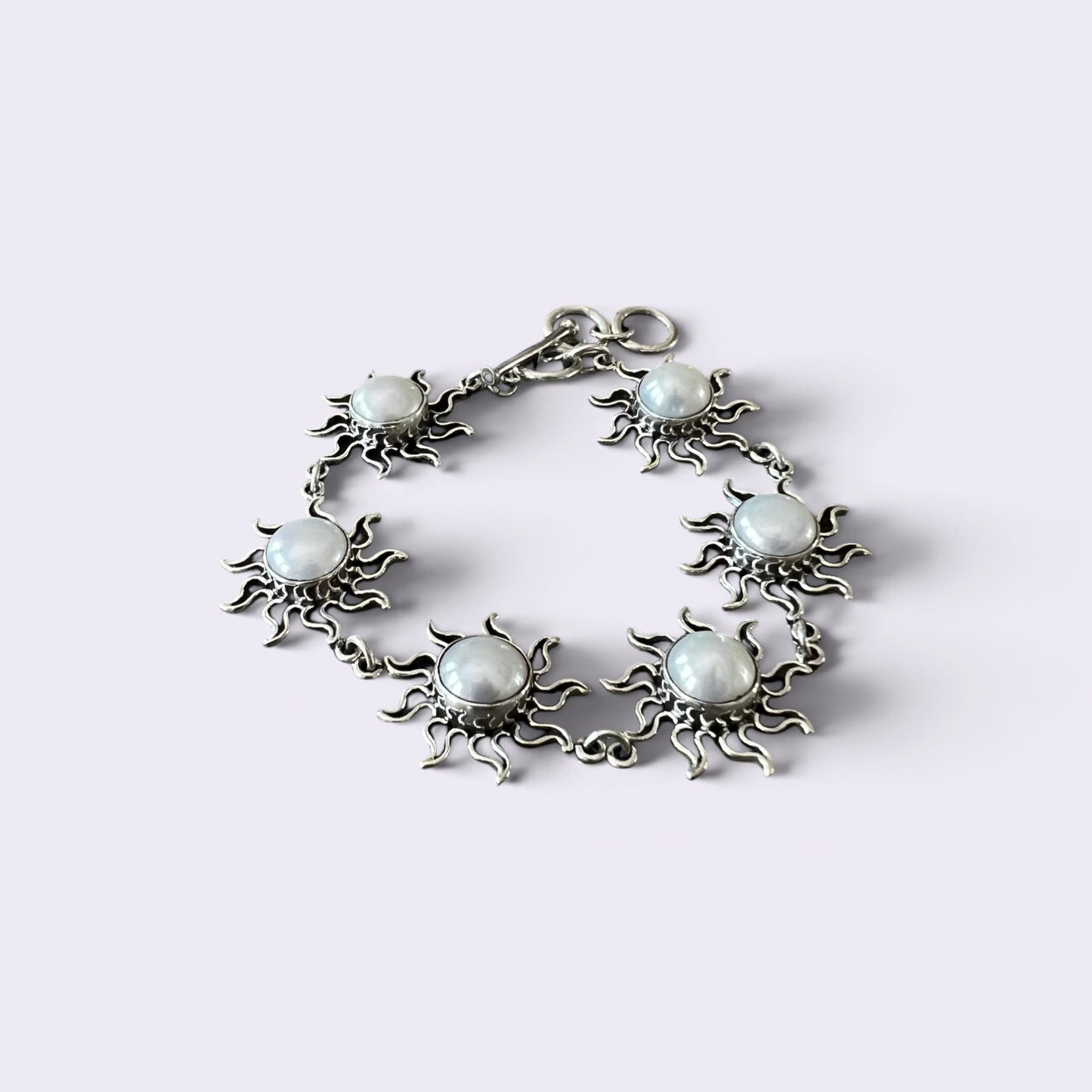 A silver-toned bracelet featuring five sun-shaped charms, each with a round, milky white stone in the center, displayed on a light lavender background.