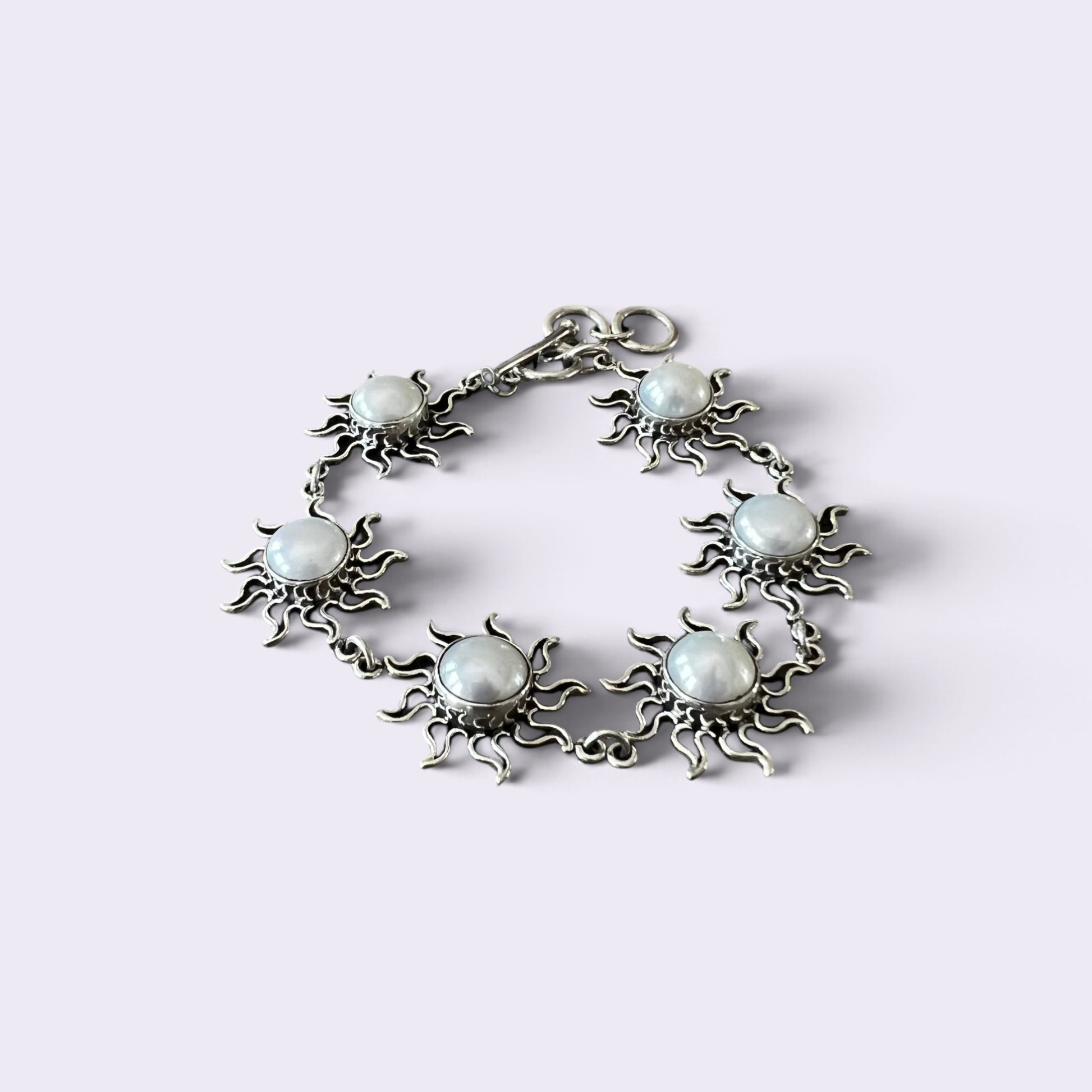 A silver-toned bracelet featuring five sun-shaped charms, each with a round, milky white stone in the center, displayed on a light lavender background.