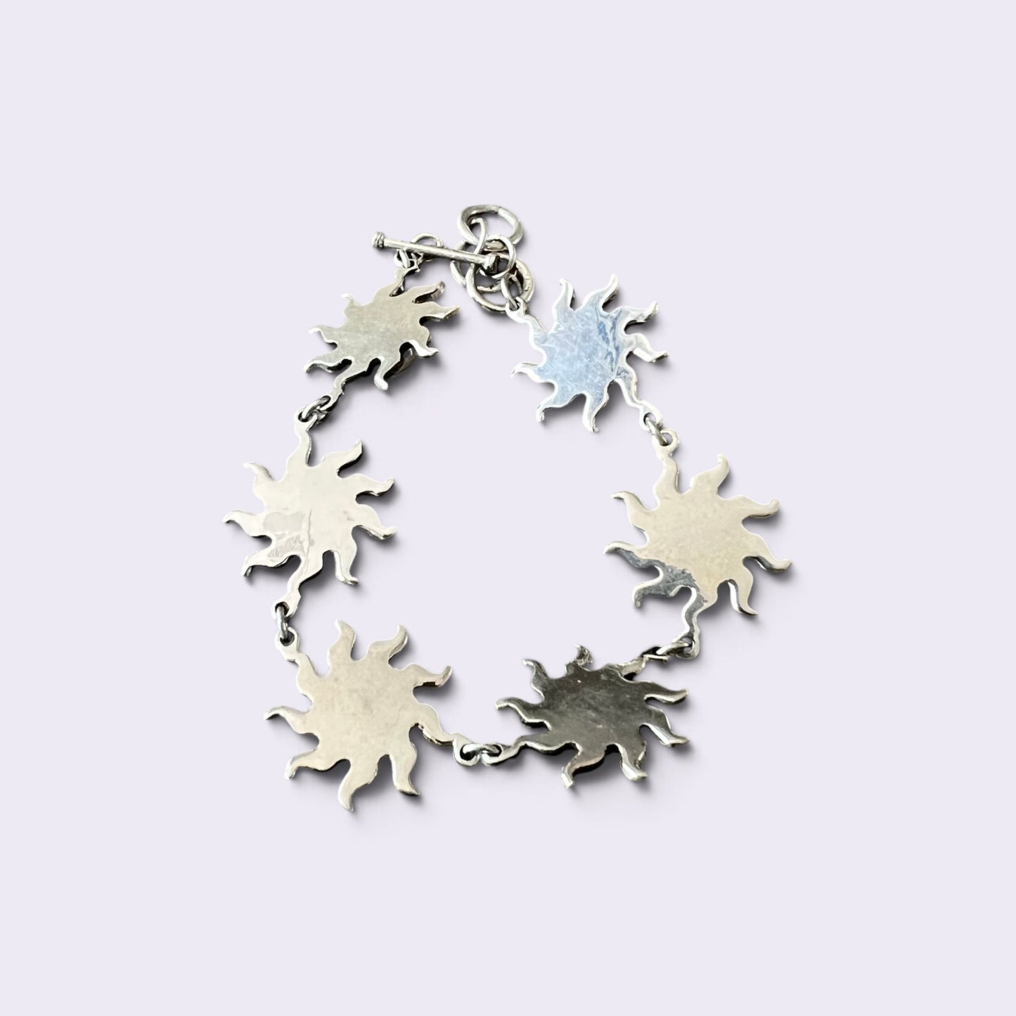 A silver sunburst charm bracelet with five textured star-shaped charms connected by delicate silver chains, shown on a light lavender background.