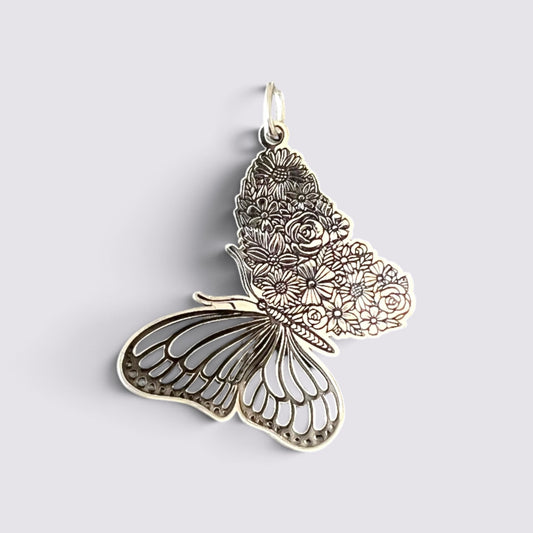 A silver butterfly pendant with intricate floral engravings on one wing and detailed wing patterns on the other, shown on a light gray background.