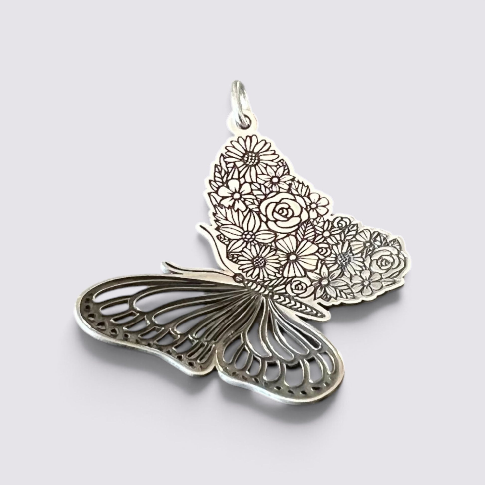 A silver butterfly-shaped pendant featuring intricate floral engravings on one wing and openwork detailing on the other, shown on a light gray background.