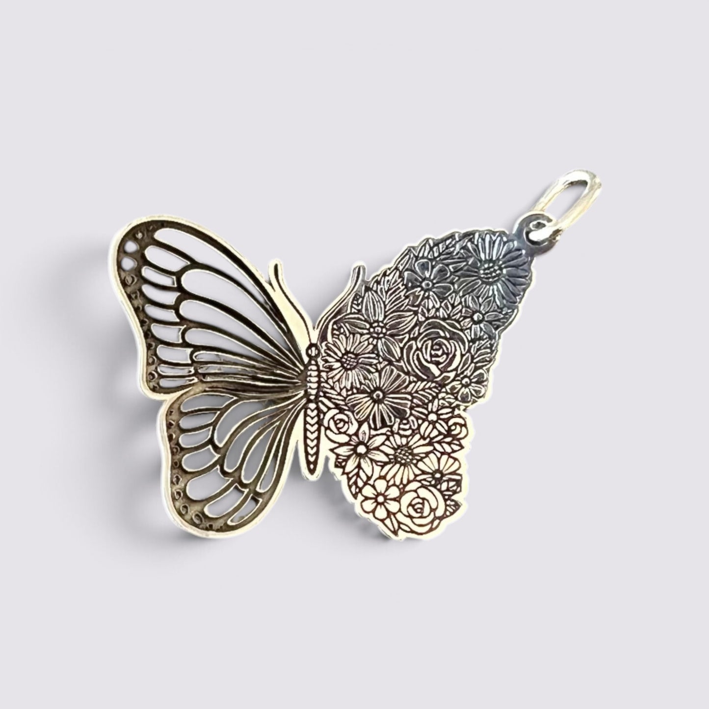 A butterfly-shaped pendant charm with a split design: one half is openwork metallic gold, and the other half is filled with engraved floral patterns in a silver-tone finish, complete with a small hanging loop at the top, shown on a light gray background.