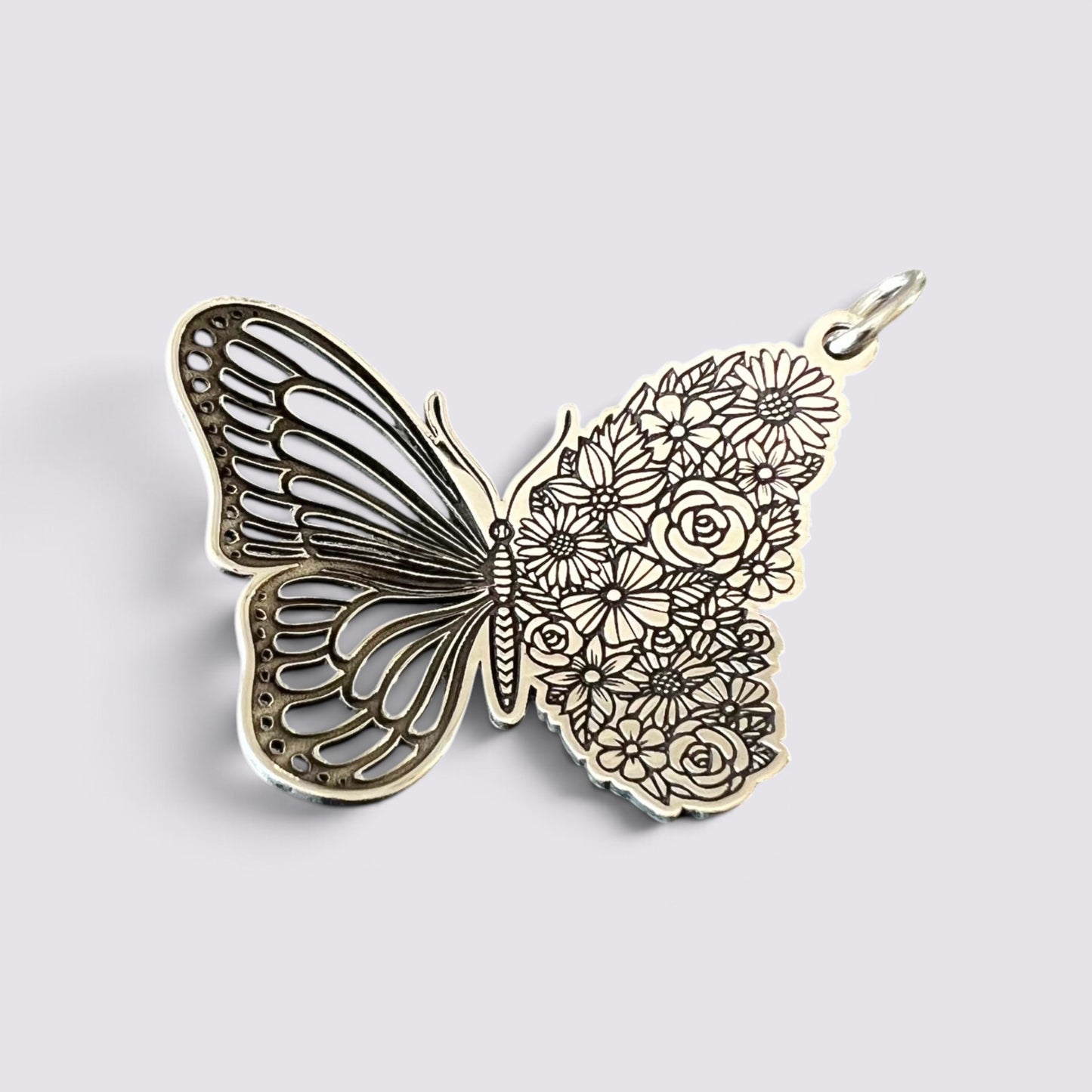 A butterfly-shaped pendant charm with intricate filigree wings on one side and floral engravings on the other, shown on a light gray background.
