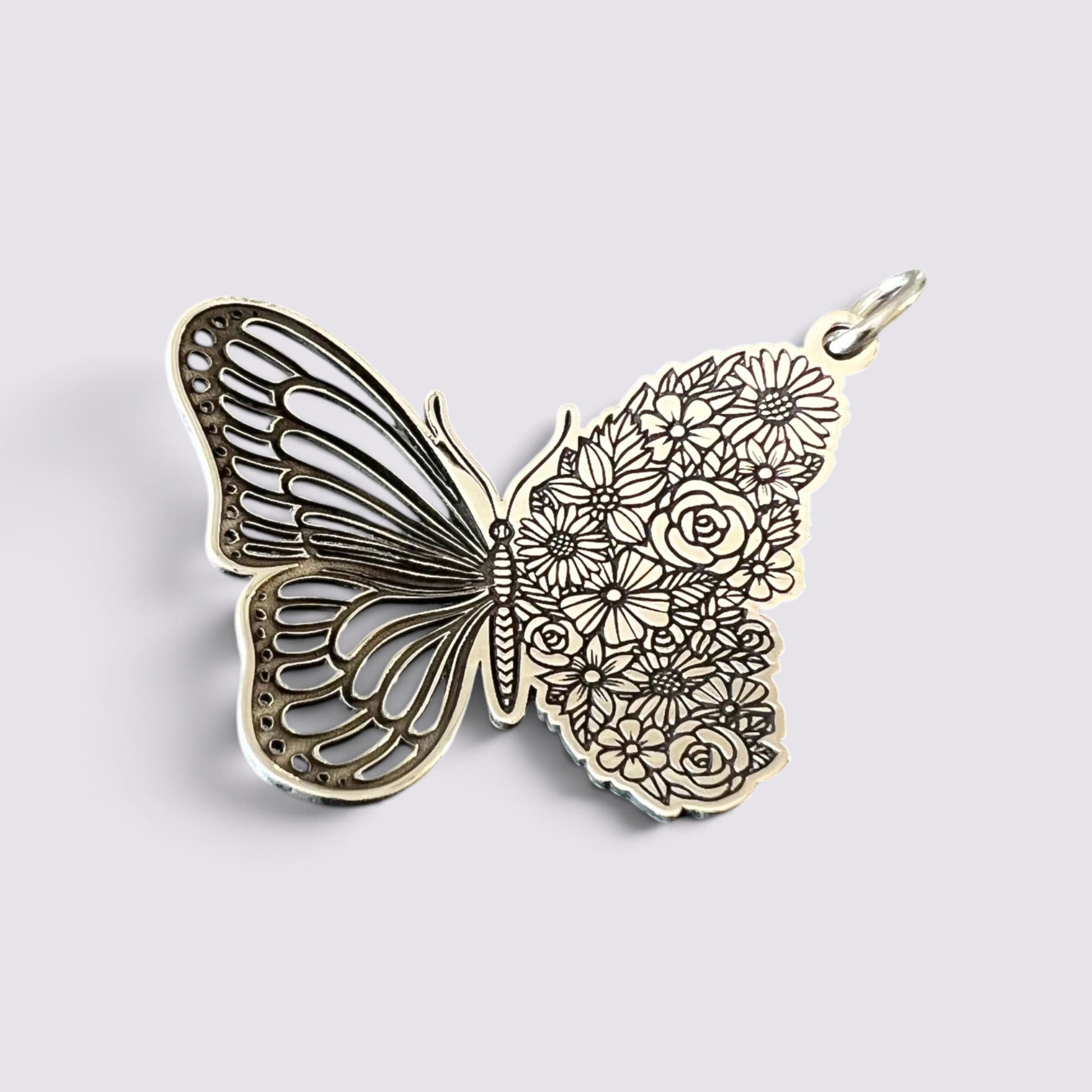 A butterfly-shaped pendant charm with intricate filigree wings on one side and floral engravings on the other, shown on a light gray background.
