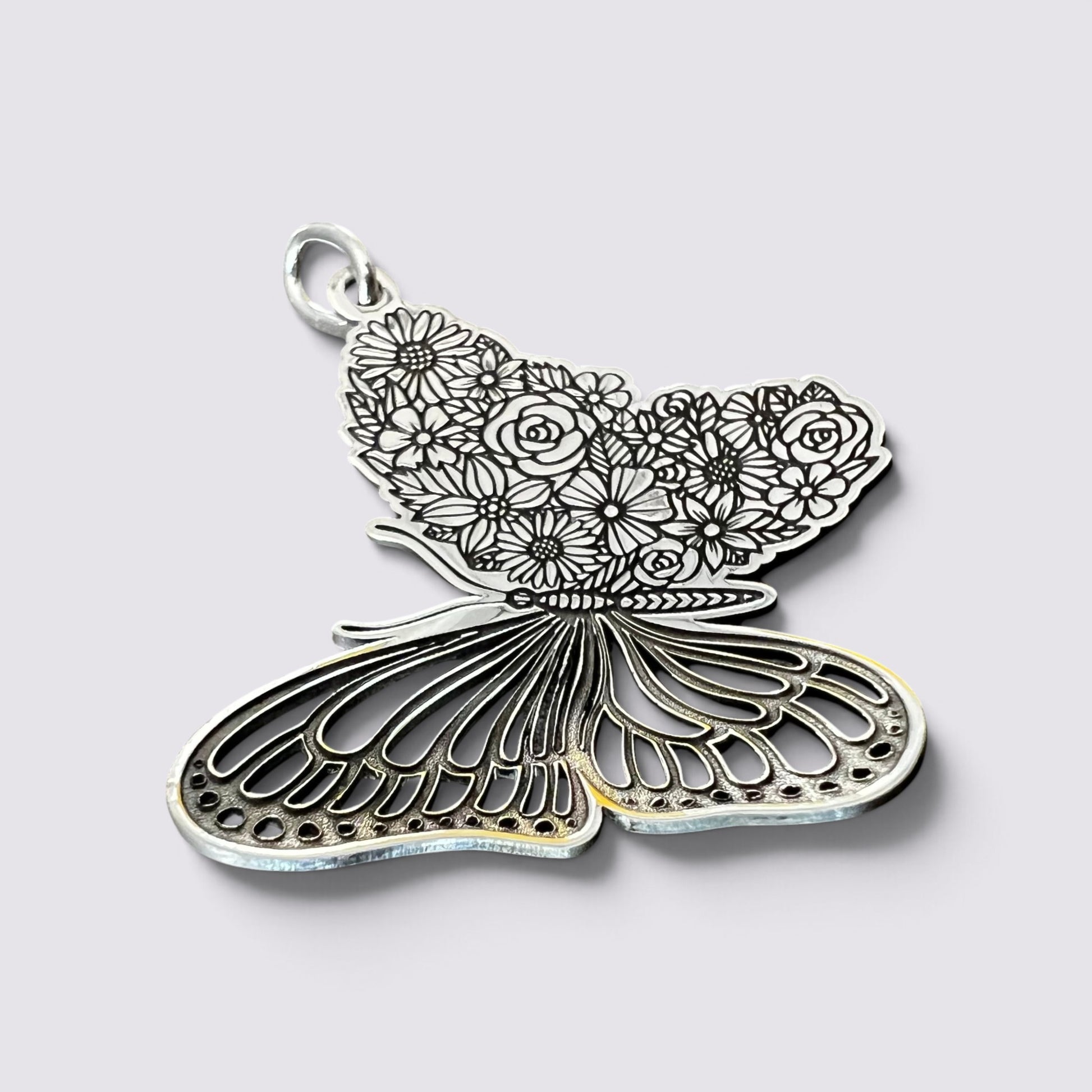 A silver butterfly-shaped pendant with intricate floral engravings on one wing and openwork detailing on the other, shown on a light gray background.