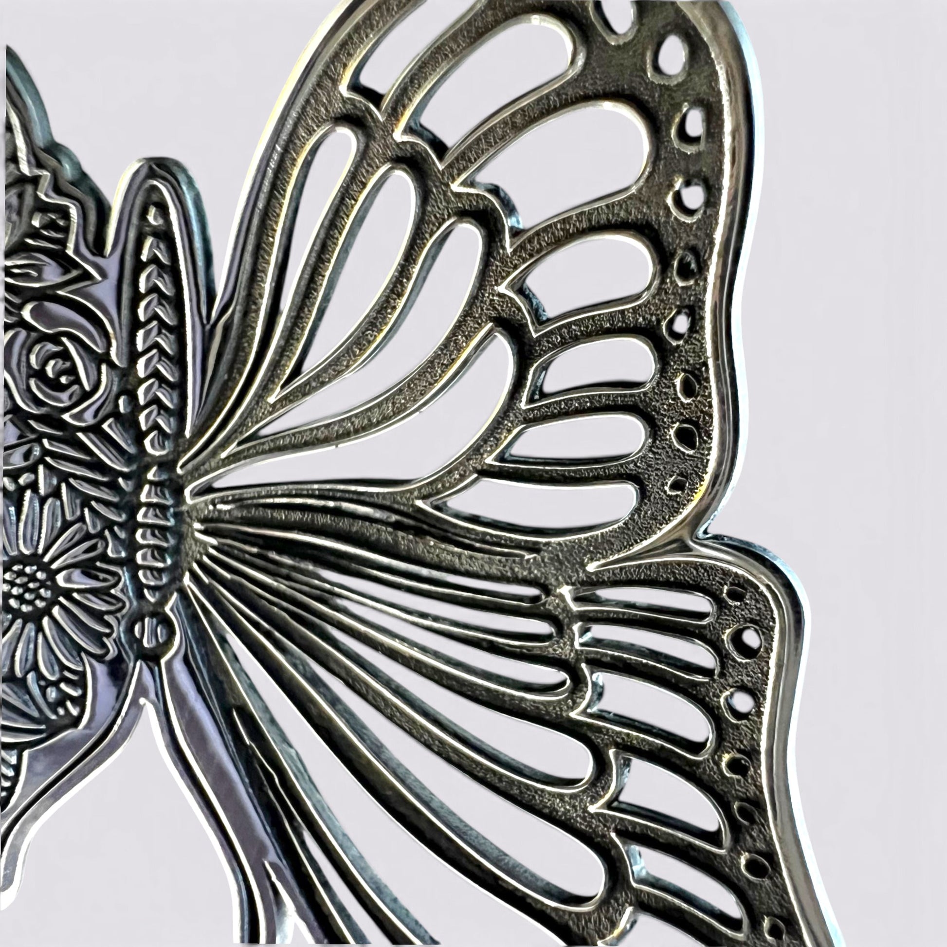 Close-up of a metallic butterfly-shaped decorative object with intricate cutout wing patterns and engraved floral details, shown against a plain light background.