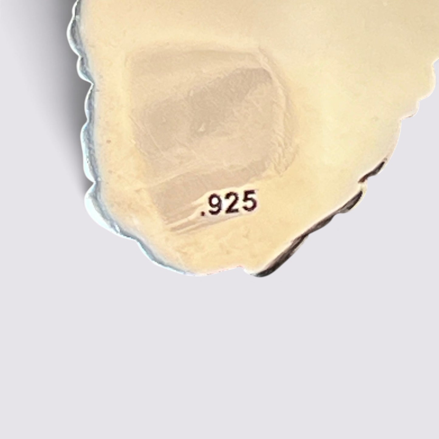 A close-up of a polished irregularly shaped stone or crystal fragment with the decimal number .925 printed on it, set against a plain light gray background.