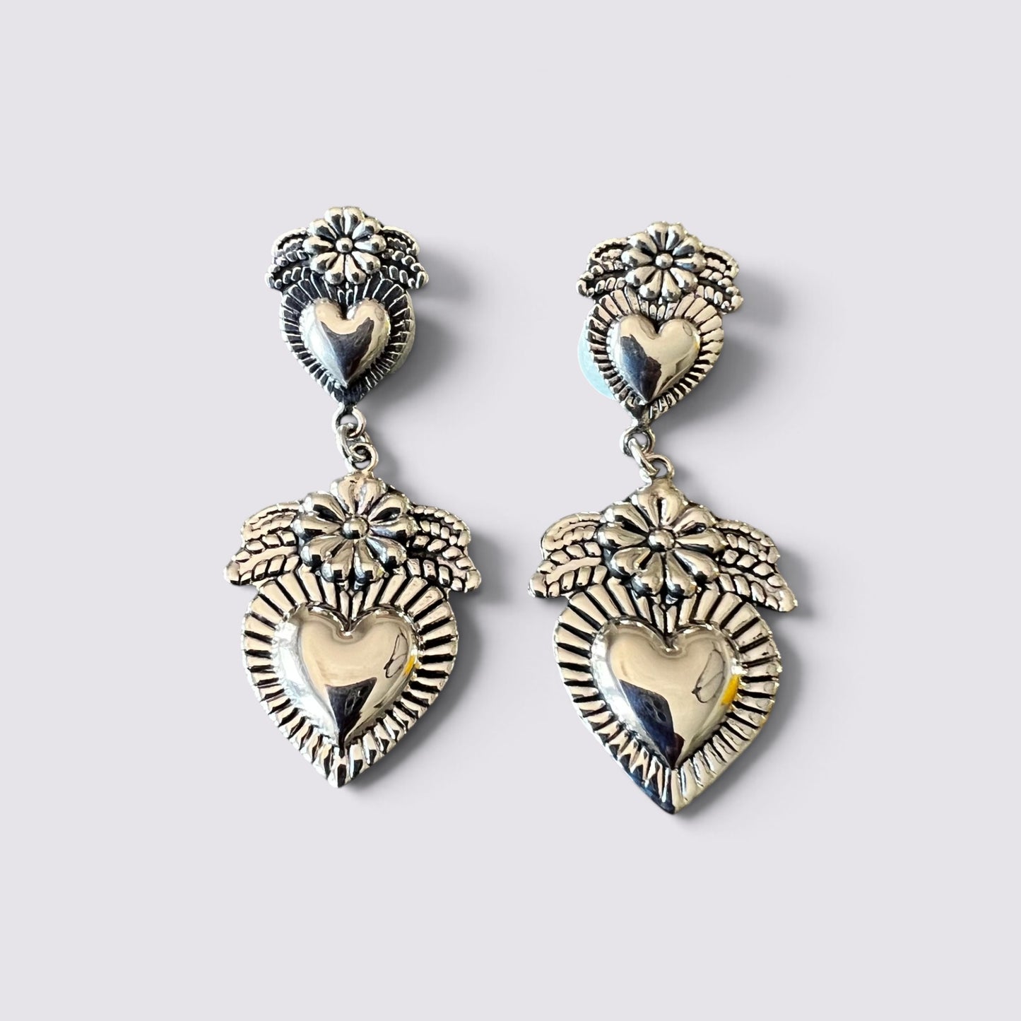 A pair of silver-toned dangle earrings featuring a central heart motif surrounded by floral and leaf details, shown against a plain light gray background.