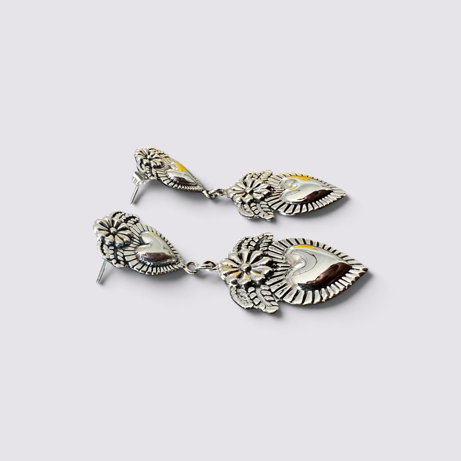 A pair of silver-toned dangle earrings with oxidized floral details and polished inlays of yellow, brown, and white stone, displayed on a light gray background.