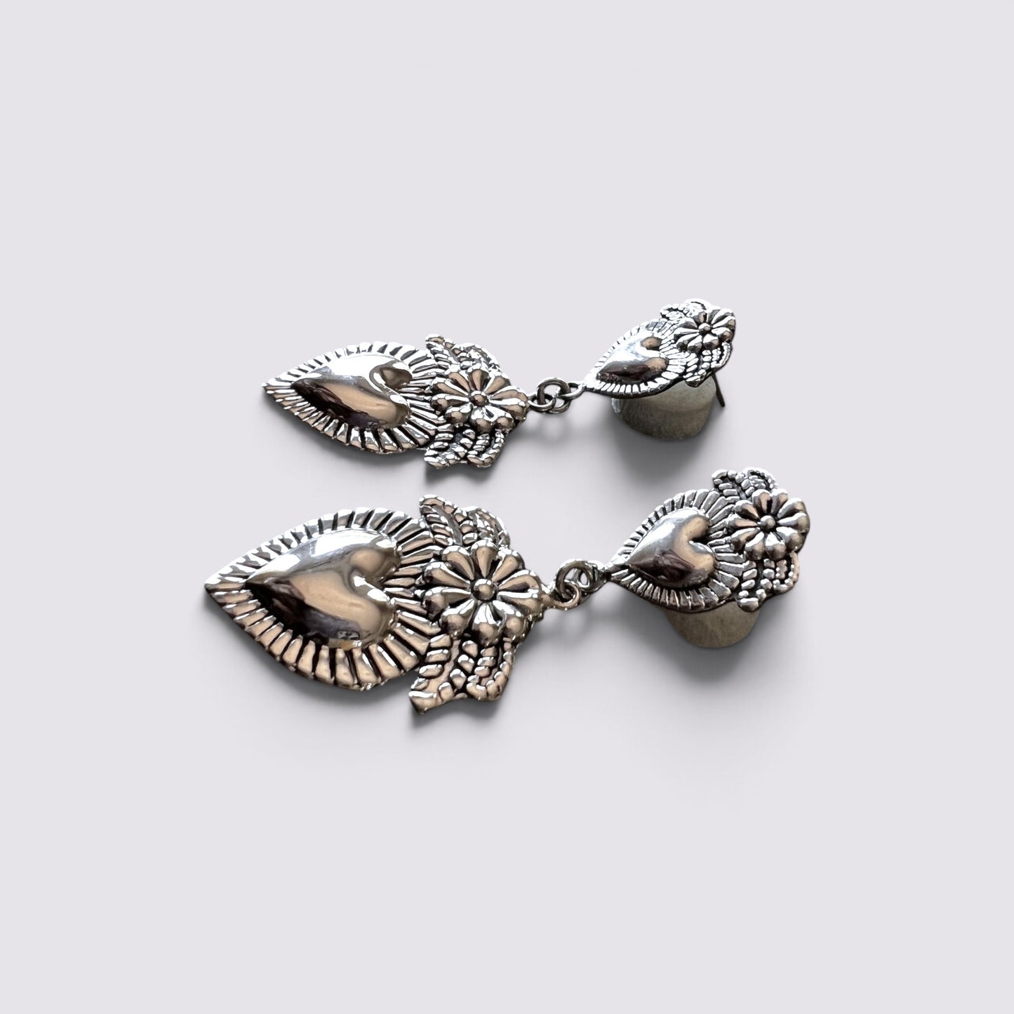 A pair of silver-toned dangle earrings with detailed leaf and floral motifs, displayed on a light gray background.