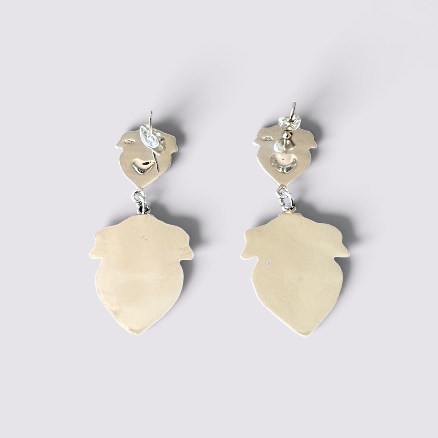 A pair of minimalist dangle earrings with irregular leaf-shaped gold pendants and small heart-shaped gold hooks, shown on a light gray background.
