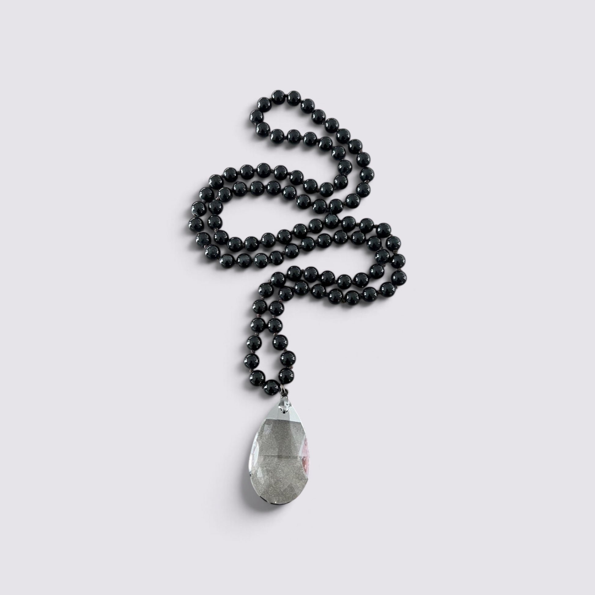 The Fashion Jewels long necklace with smooth black beads and a large clear glass teardrop pendant on a light background