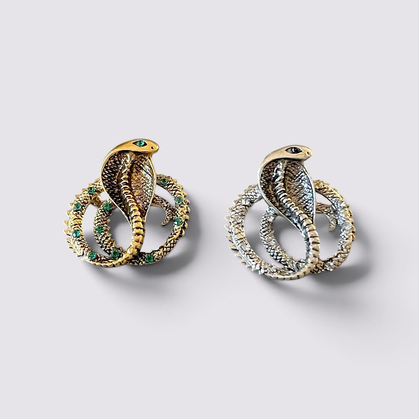 The Fashion Jewels cobra serpent statement brooch pins in gold and silver tones with sparkling green accents.
