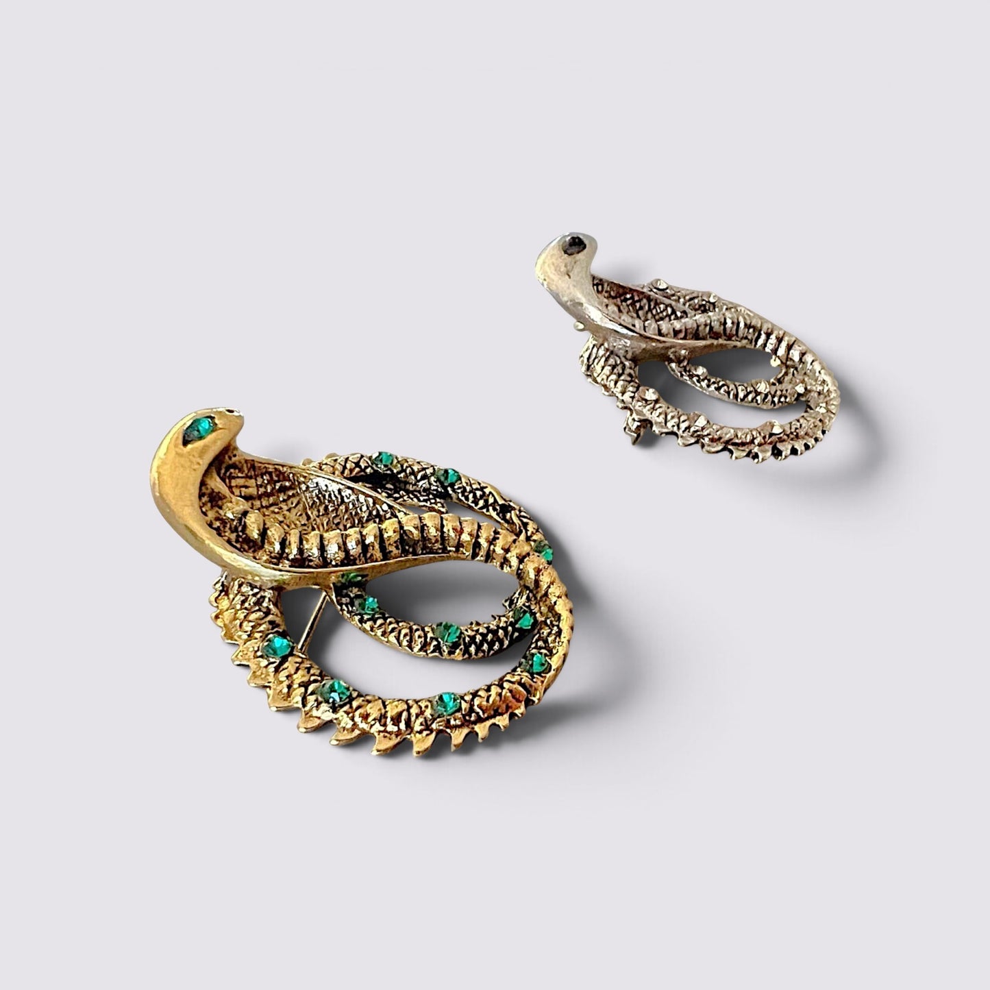 The Fashion Jewels cobra serpent statement brooch pins in gold and silver tones with sparkling green crystal accents.