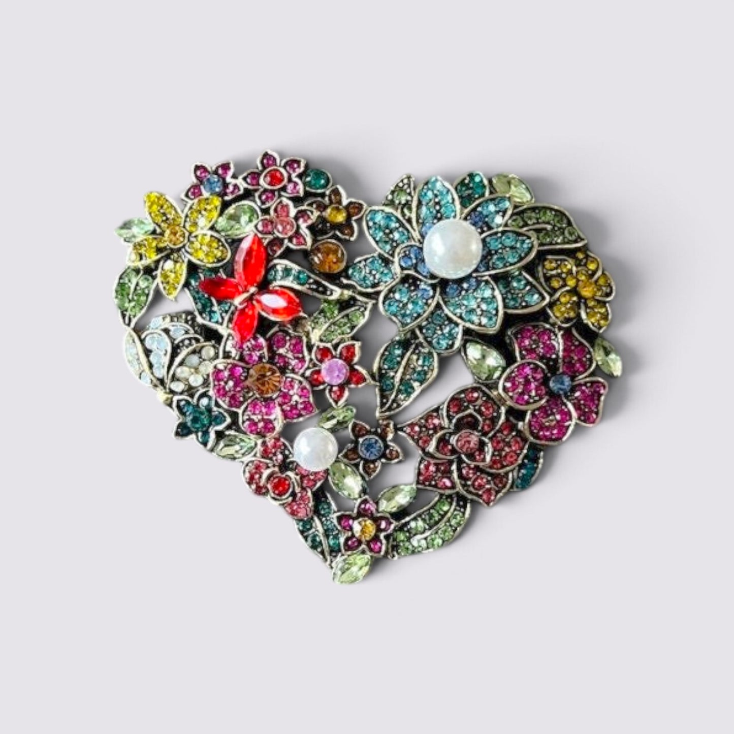 The Fashion Jewels heart-shaped brooch featuring multi-colored crystals, floral motifs, and elegant faux pearl accents.