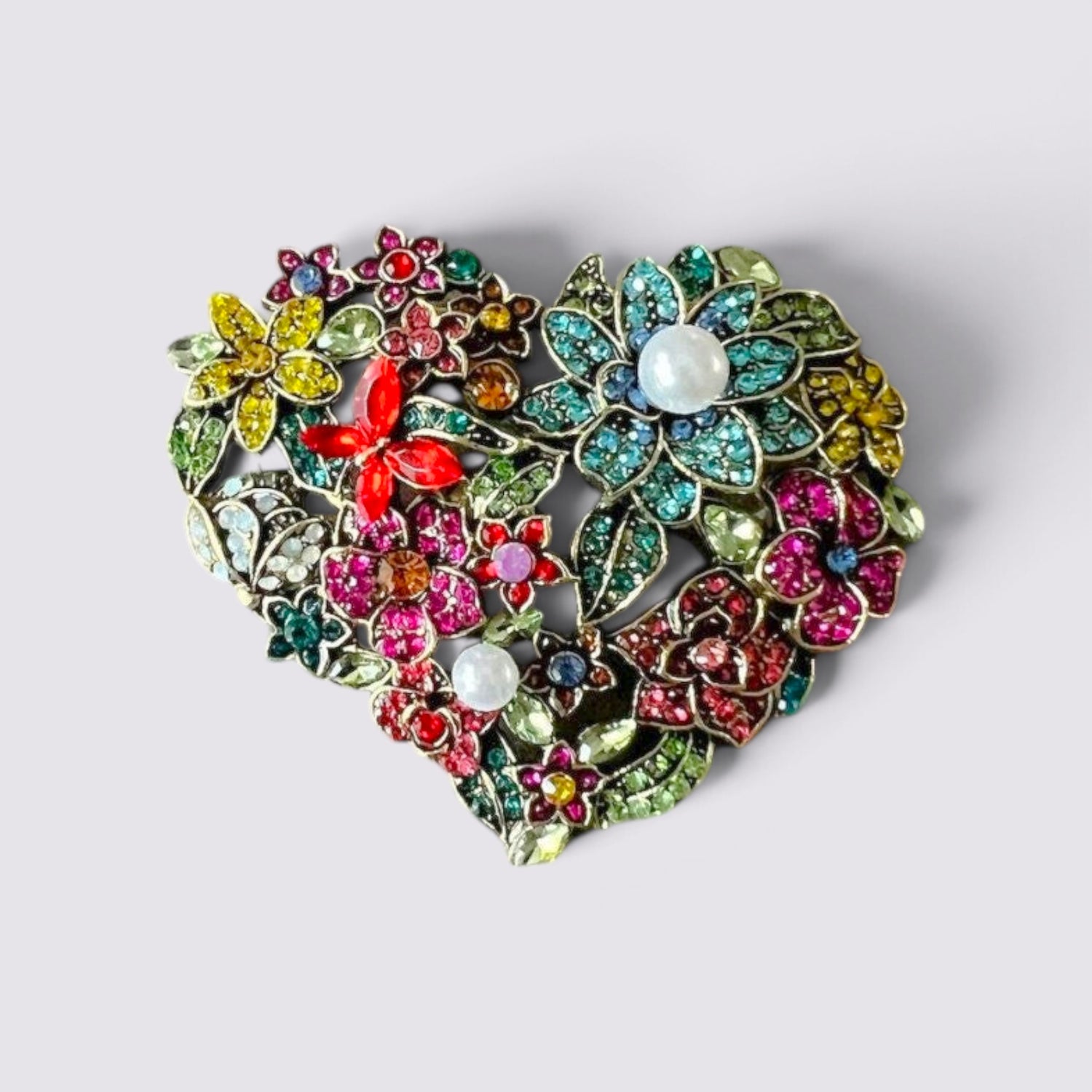 The Fashion Jewels heart-shaped brooch featuring multi-colored floral crystals and faux pearl accents in antique metal.