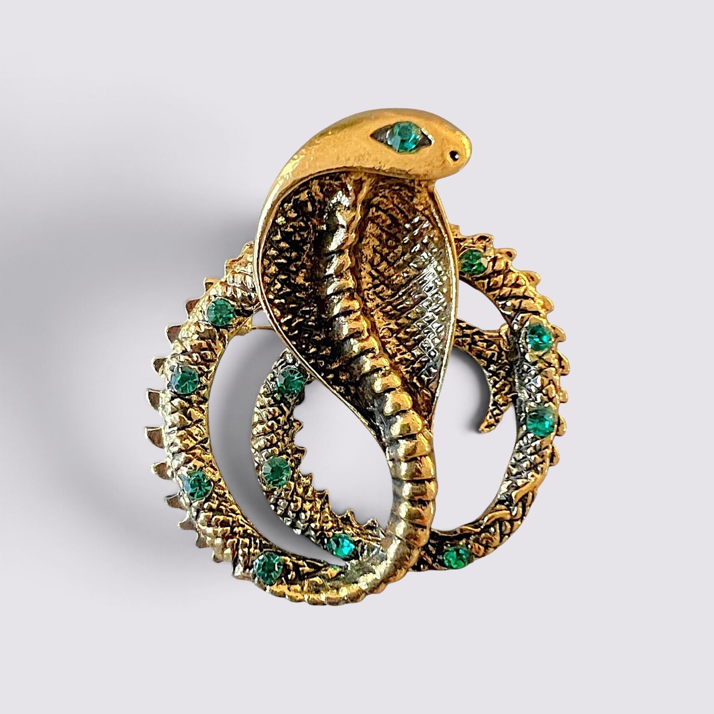 The Fashion Jewels gold cobra serpent brooch pin with green crystal accents and intricate textured scale detailing.