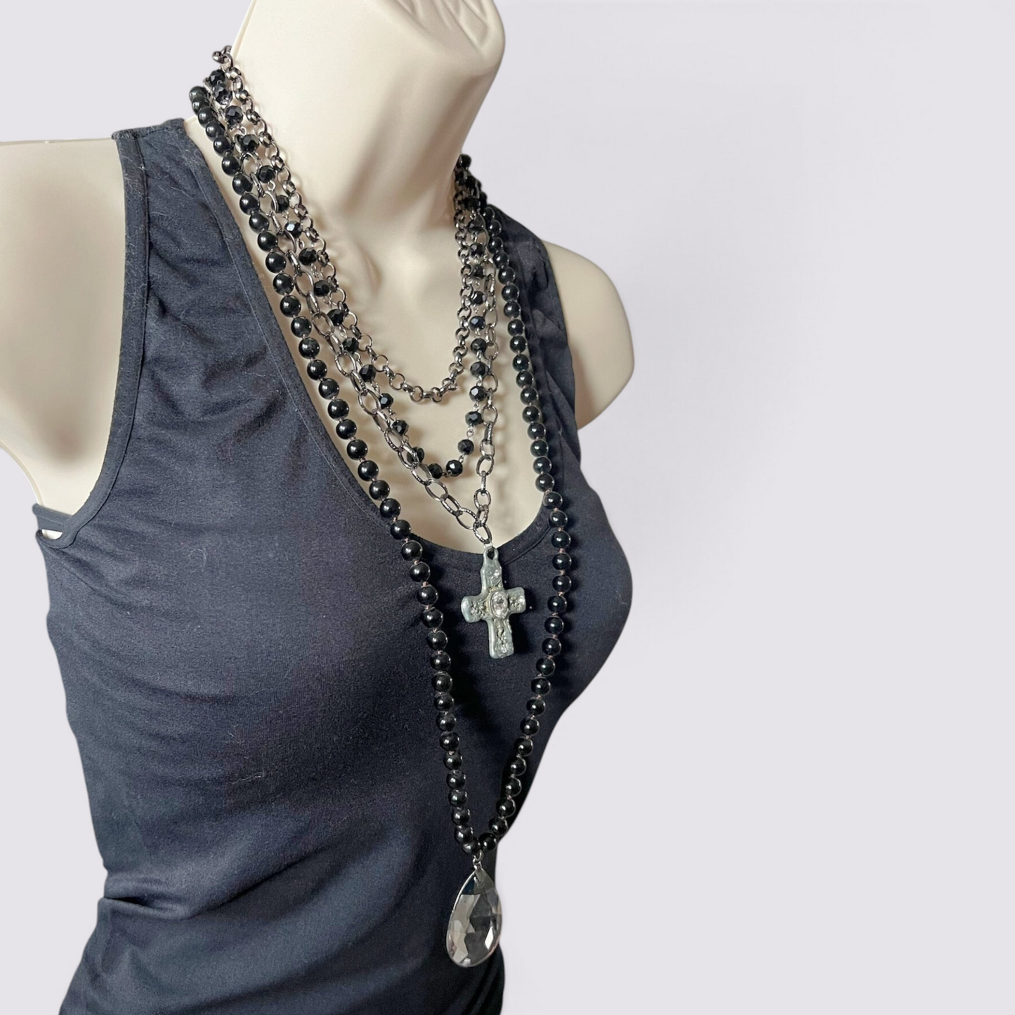 The Fashion Jewels layered necklace set featuring black beads, silver chains, a crystal cross, and a teardrop pendant.