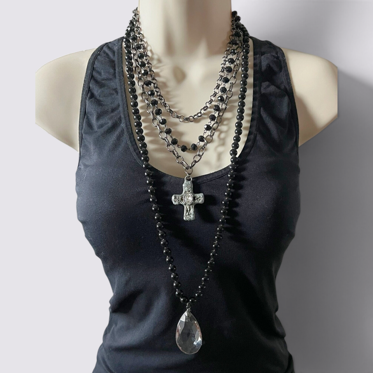 The Fashion Jewels layered necklace set featuring black beads, a crystal cross pendant, and a clear glass teardrop.