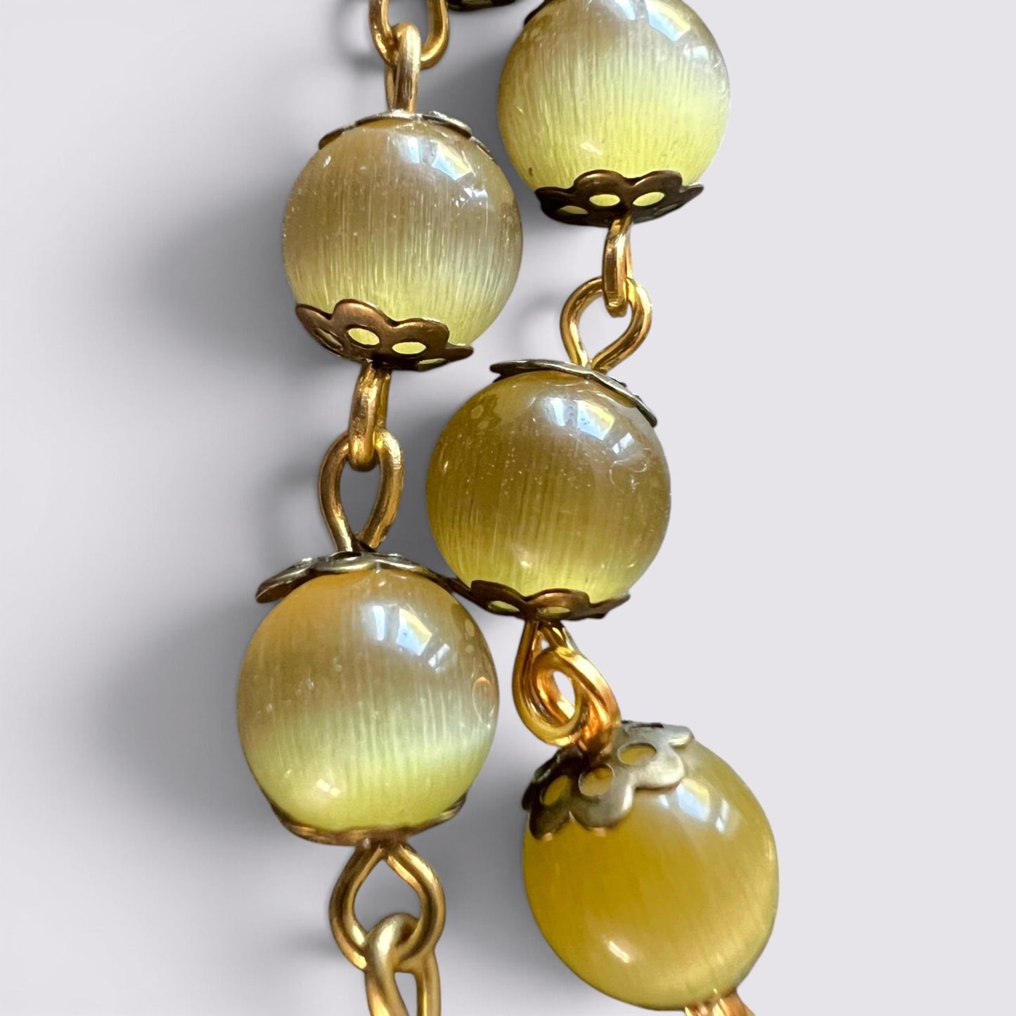 The Fashion Jewels rosary featuring luminous olive cat's eye beads with antique gold metal caps and gold-toned chain.