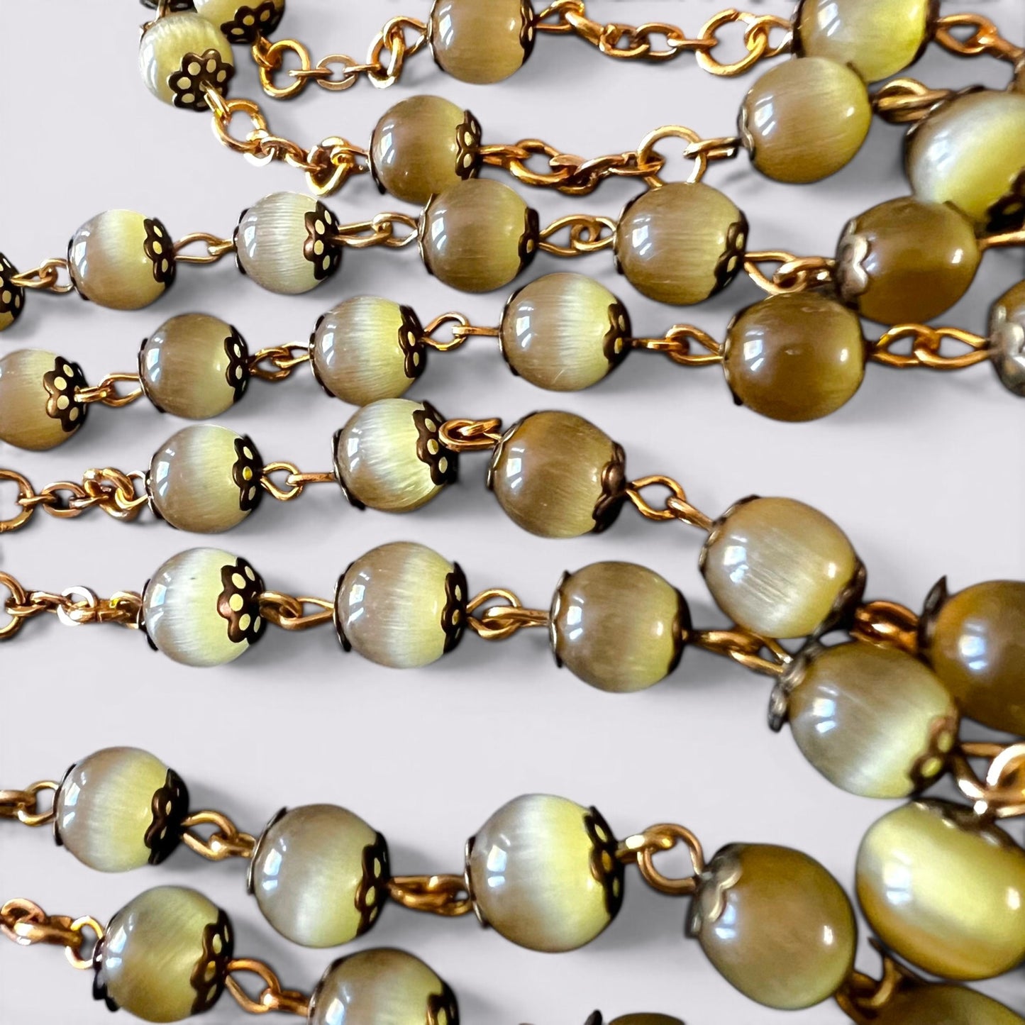 The Fashion Jewels rosary featuring olive-toned cat's eye beads with antique metal caps on a gold-toned chain.