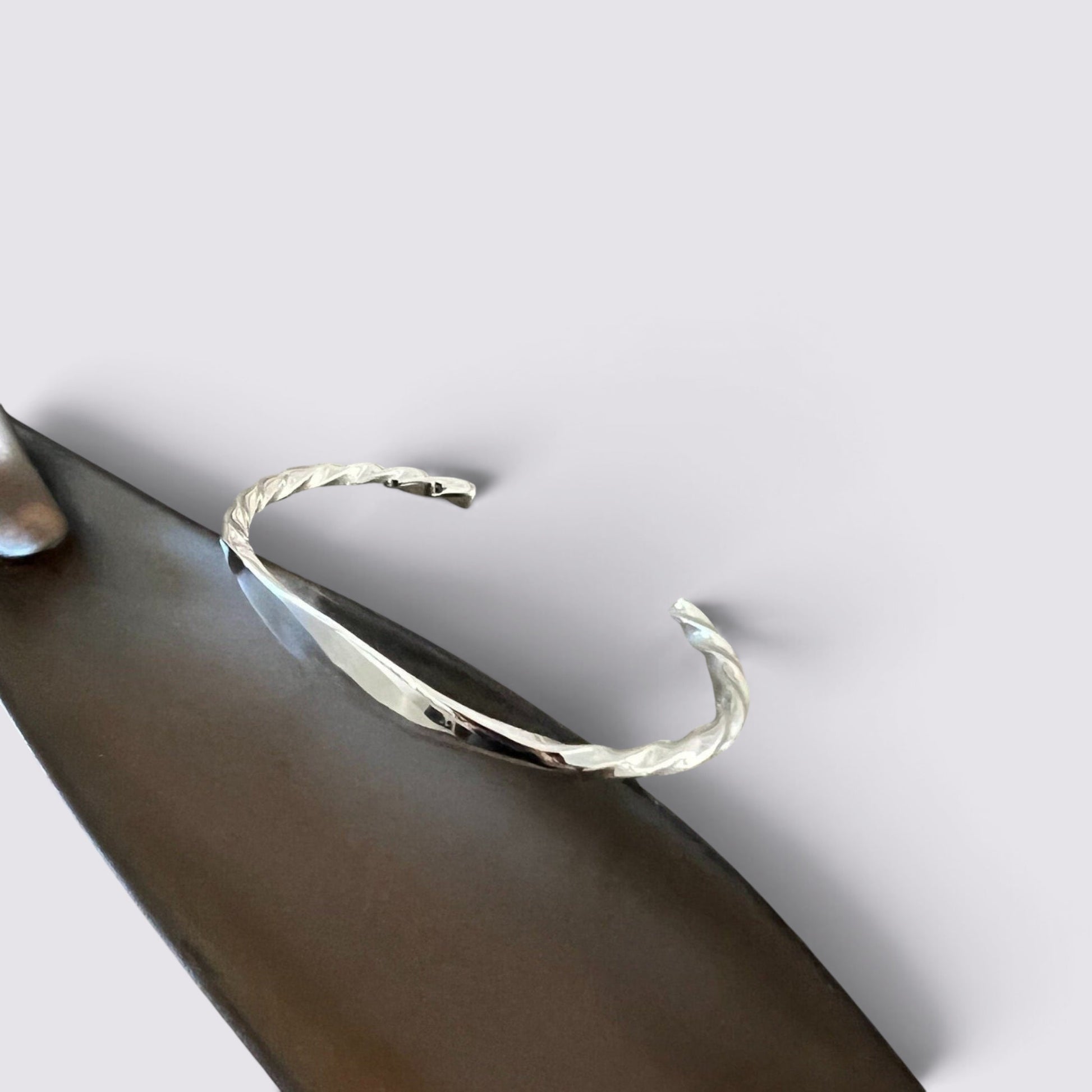 The Fashion Jewels sterling silver open cuff bracelet with a polished twisted texture on a dark display stand.