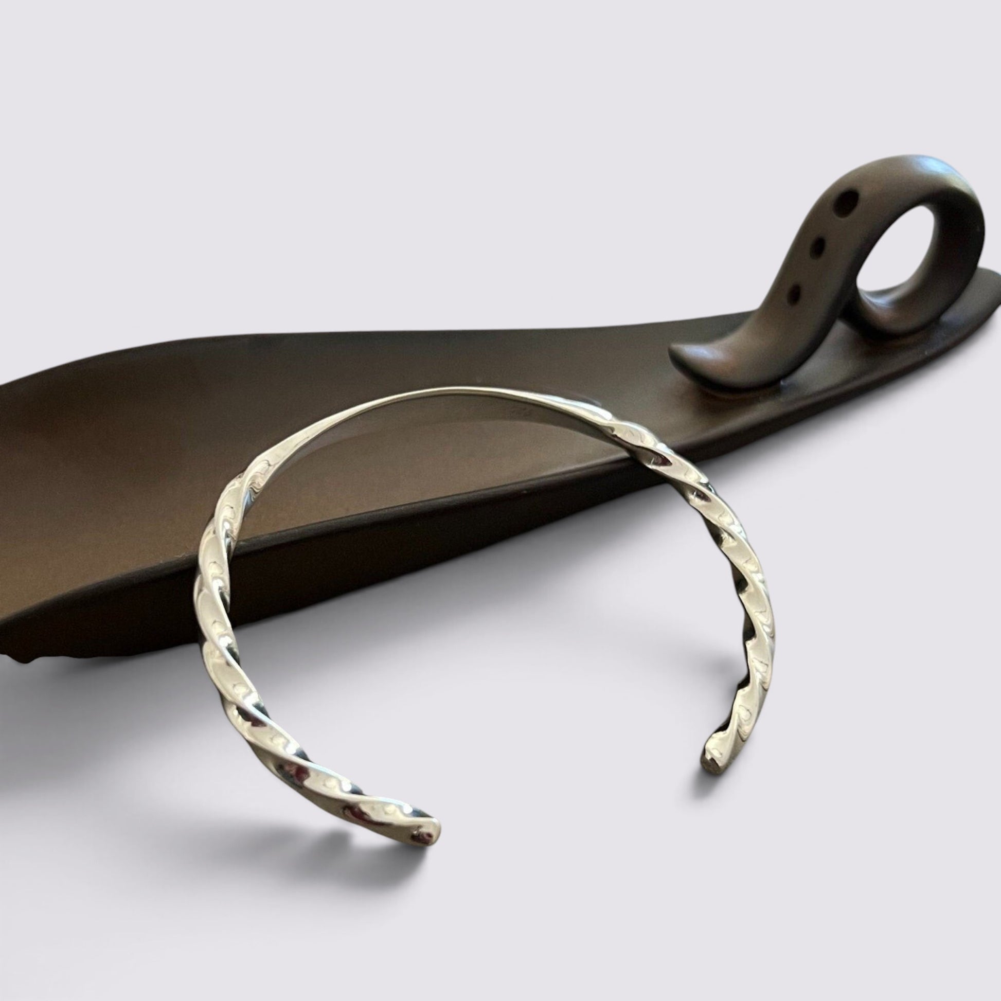 The Fashion Jewels sterling silver open-cuff bracelet with a polished twisted metal texture on a dark display stand.